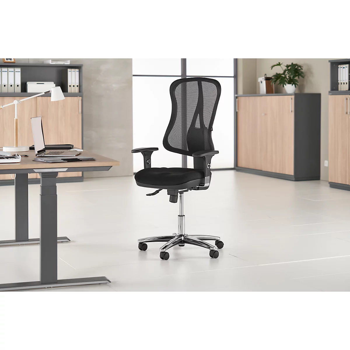 Chaise de bureau noire sur fond clair. La chaise a un dossier en maille, des accoudoirs et un piètement chromé.