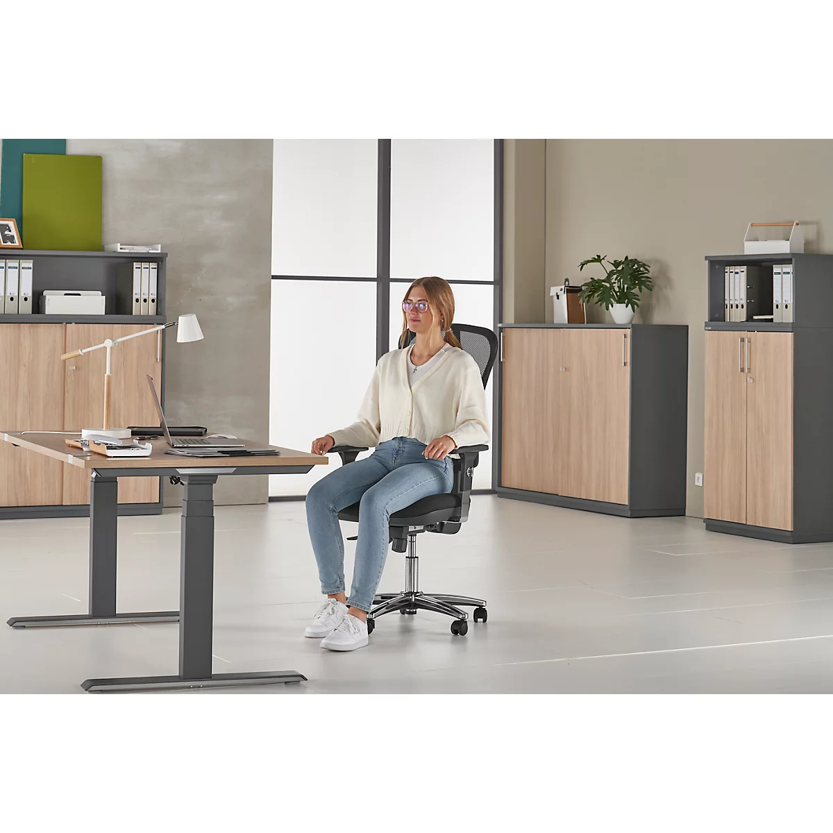 Jeune femme au bureau, assise à son bureau. Elle est assise sur une chaise de bureau. Il y a un ordinateur portable sur la table.