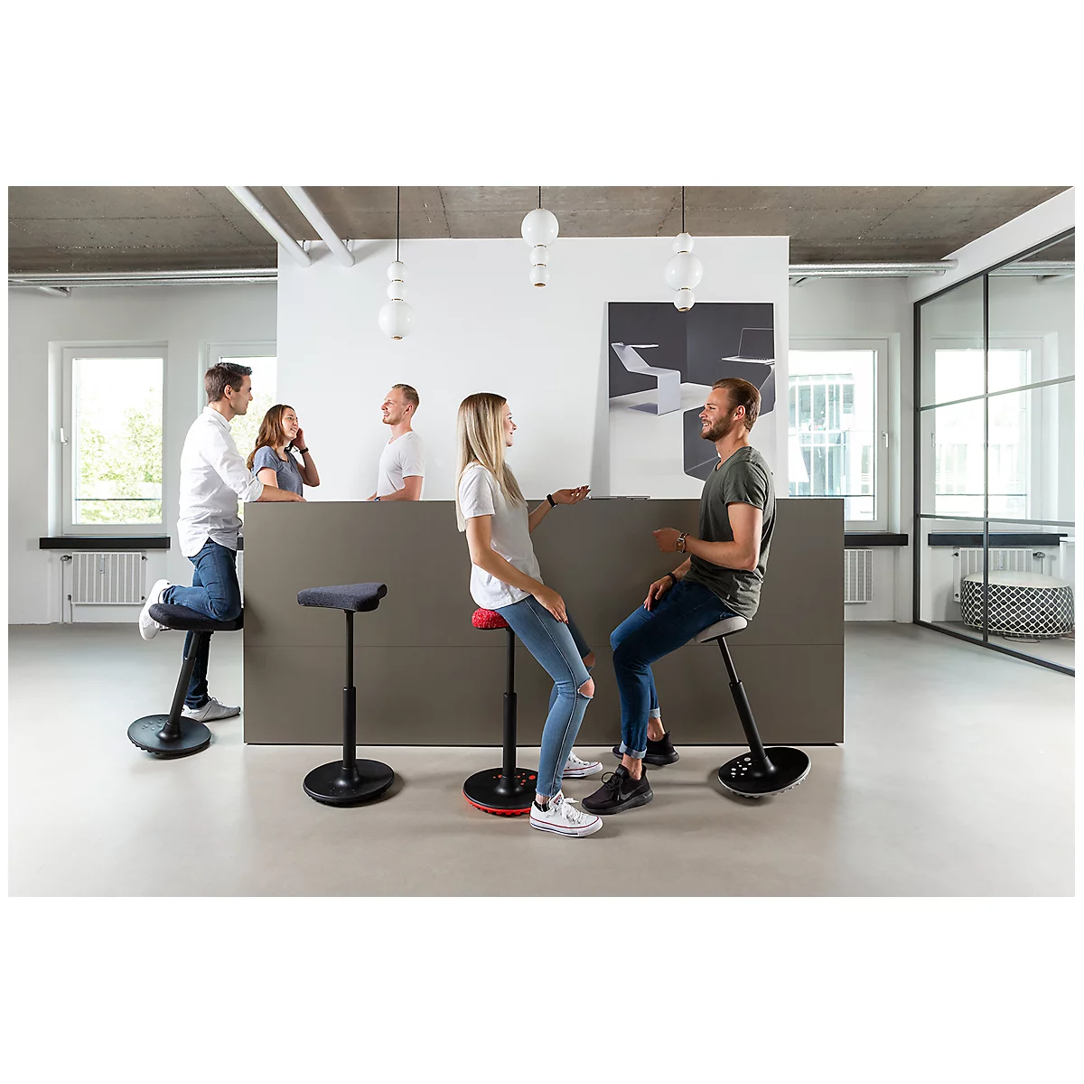 Office scene: People sit and stand at a counter on height-adjustable stools. A man and a woman are having a lively conversation.