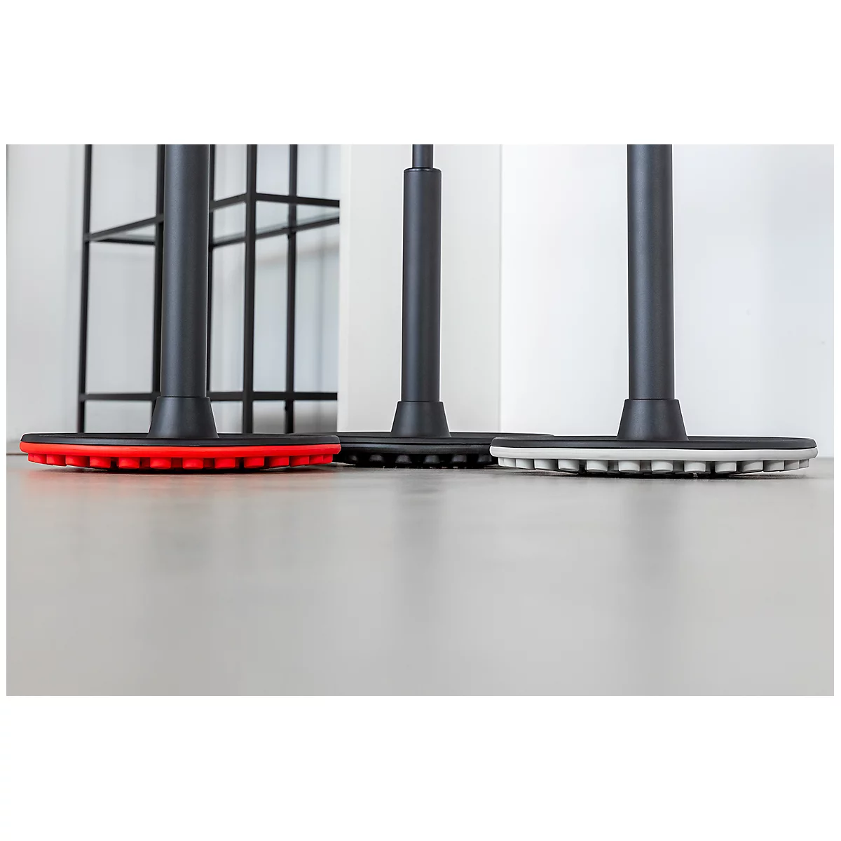 Three chair legs with colored bases, red, black, and white. The floor reflects the light.