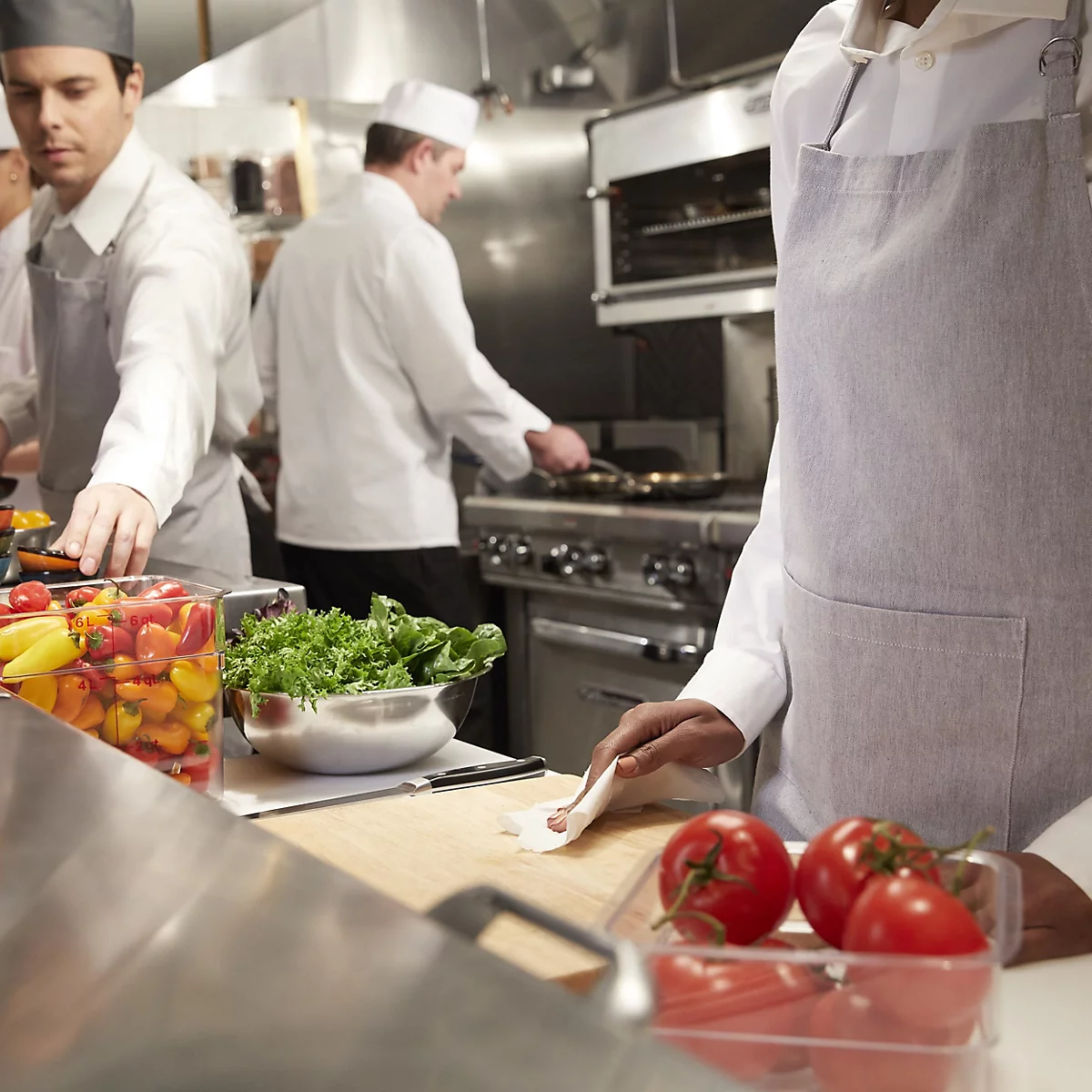 Chefs travaillant dans une cuisine. Tomates et salade sur le comptoir.