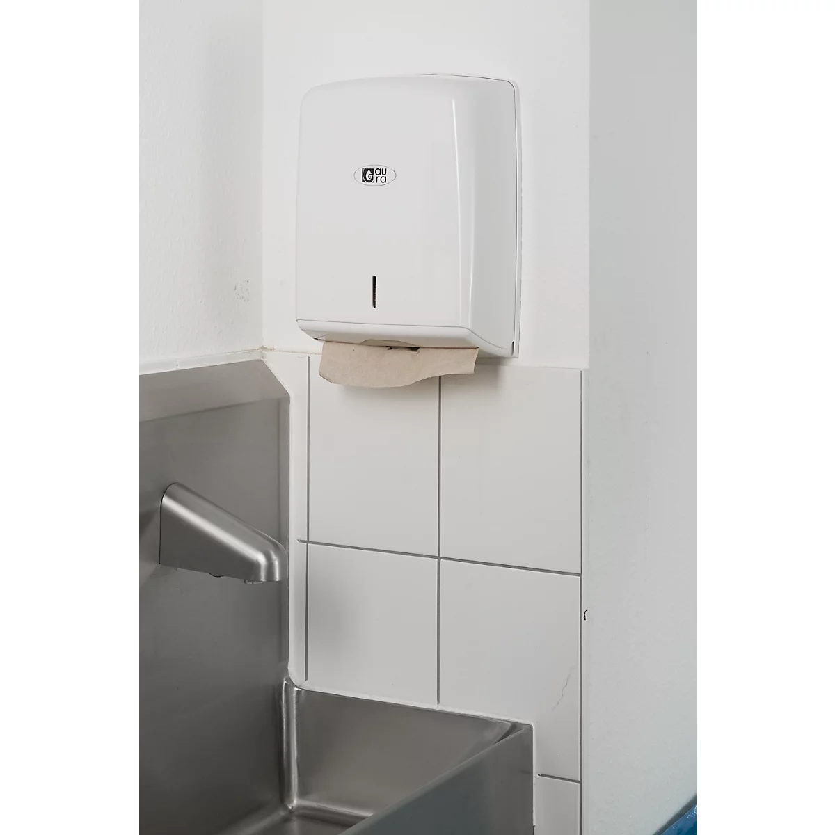 White paper towel dispenser on white wall, above a stainless steel sink. A paper towel is hanging out.