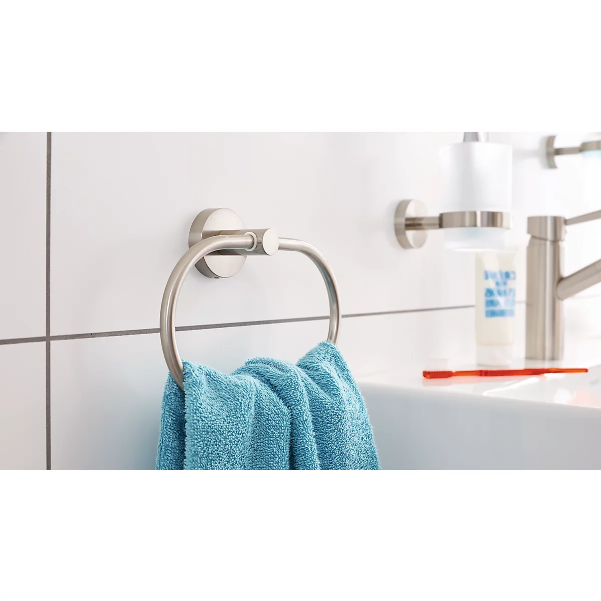 Metal towel ring with blue towel, next to a sink with soap dispenser and faucet.