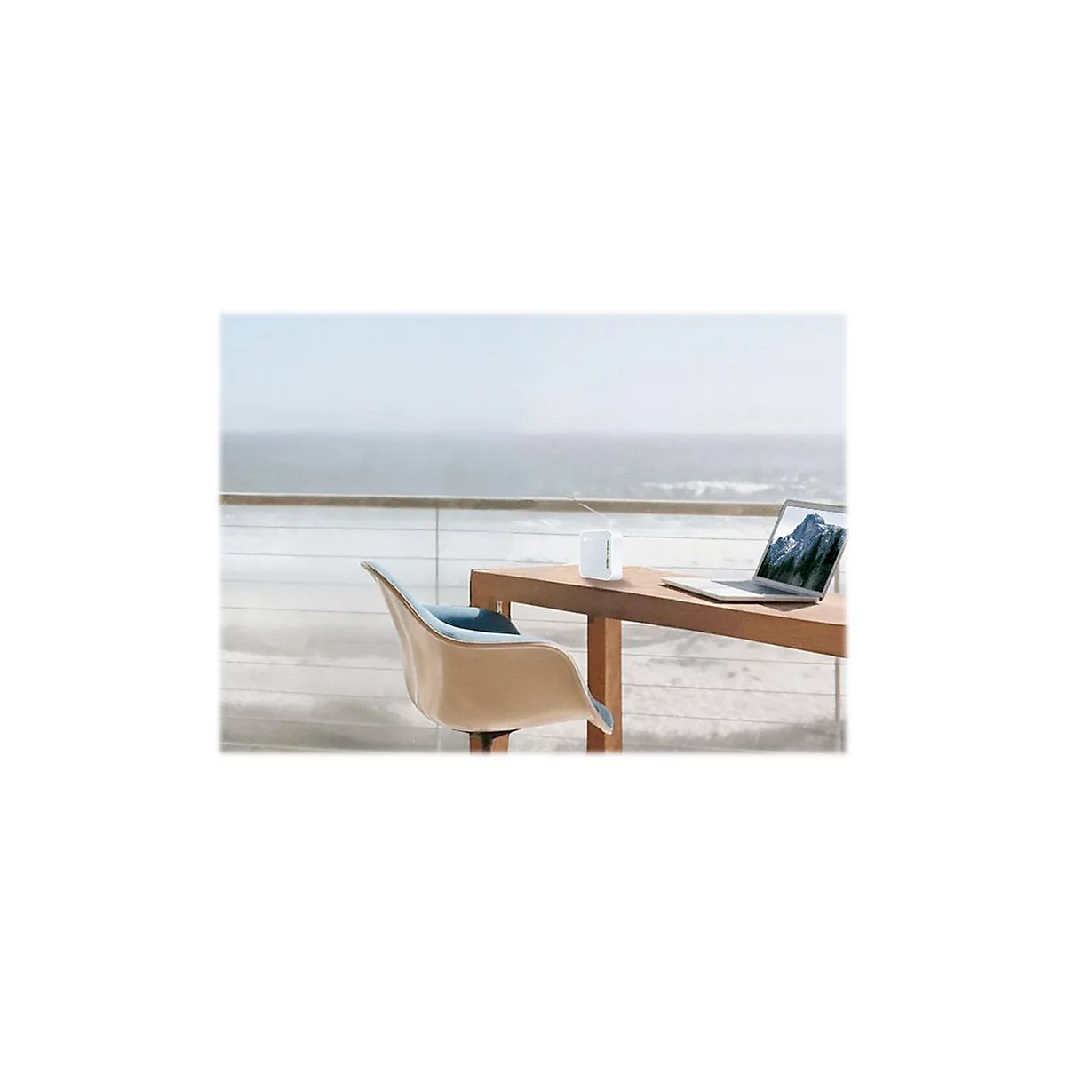 Ein Laptop und ein WLAN-Router stehen auf einem Holztisch, vor dem Meer. Ein Stuhl steht davor.