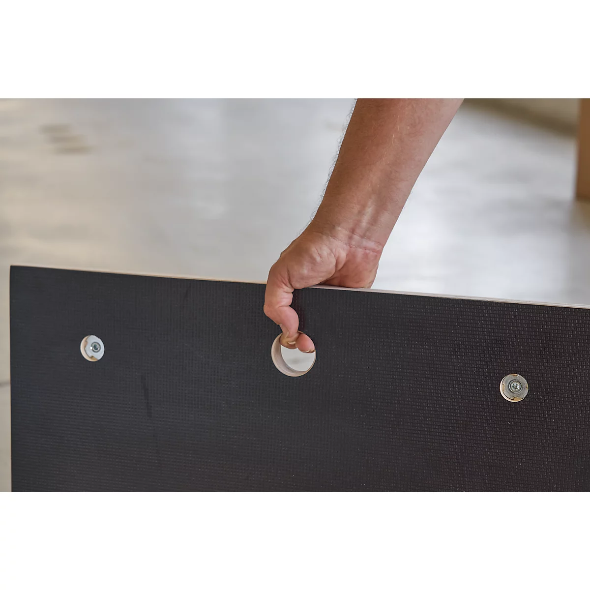 A person holds a dark wooden board with a hole. Screws are attached.