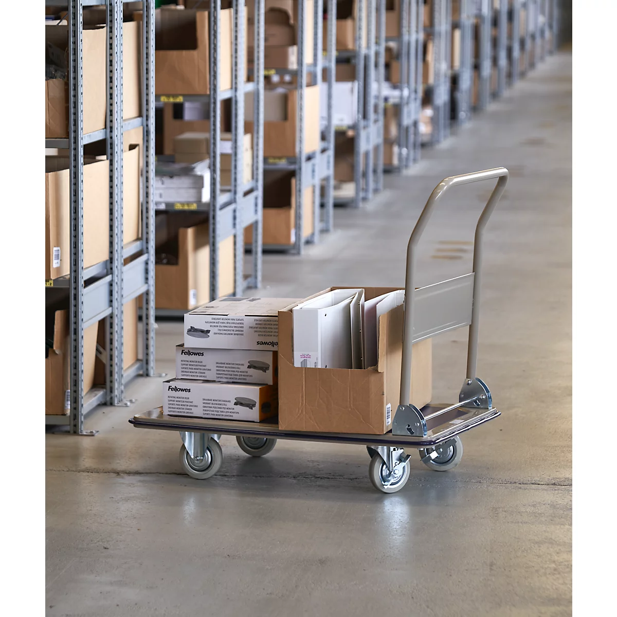 A transport trolley with boxes and binders in a warehouse. In the background, shelves with more boxes can be seen.