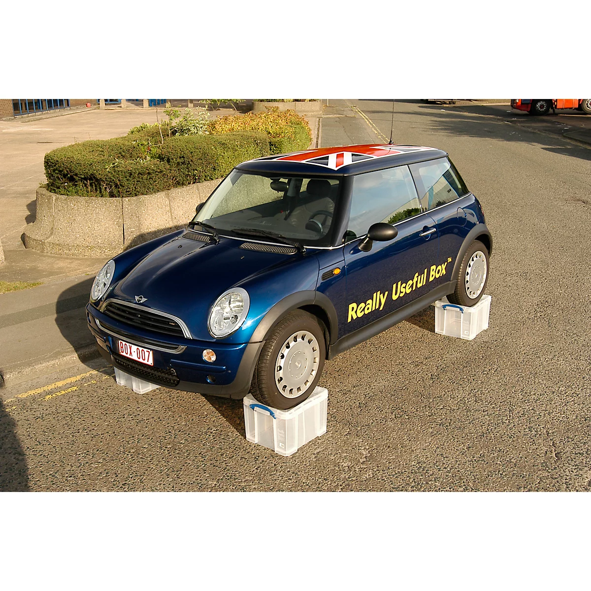 Blauwe Mini Cooper, die op dozen staat. De Britse vlag staat op het dak en 'Really Useful Box' staat op de zijkant.