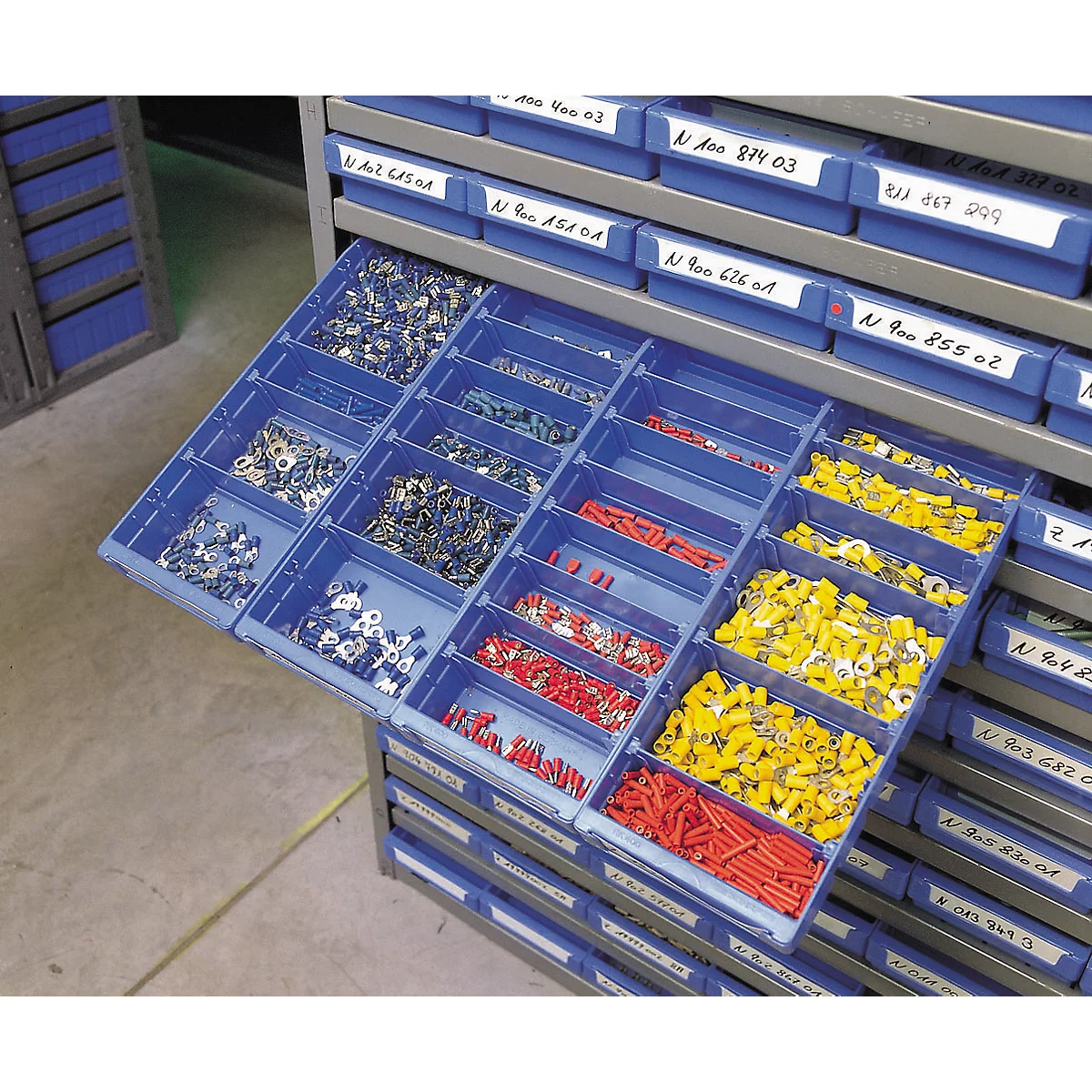 Geöffnete Schublade eines Werkstattschranks mit beschrifteten blauen Kunststoffboxen voller bunter Kabelschuhe.
