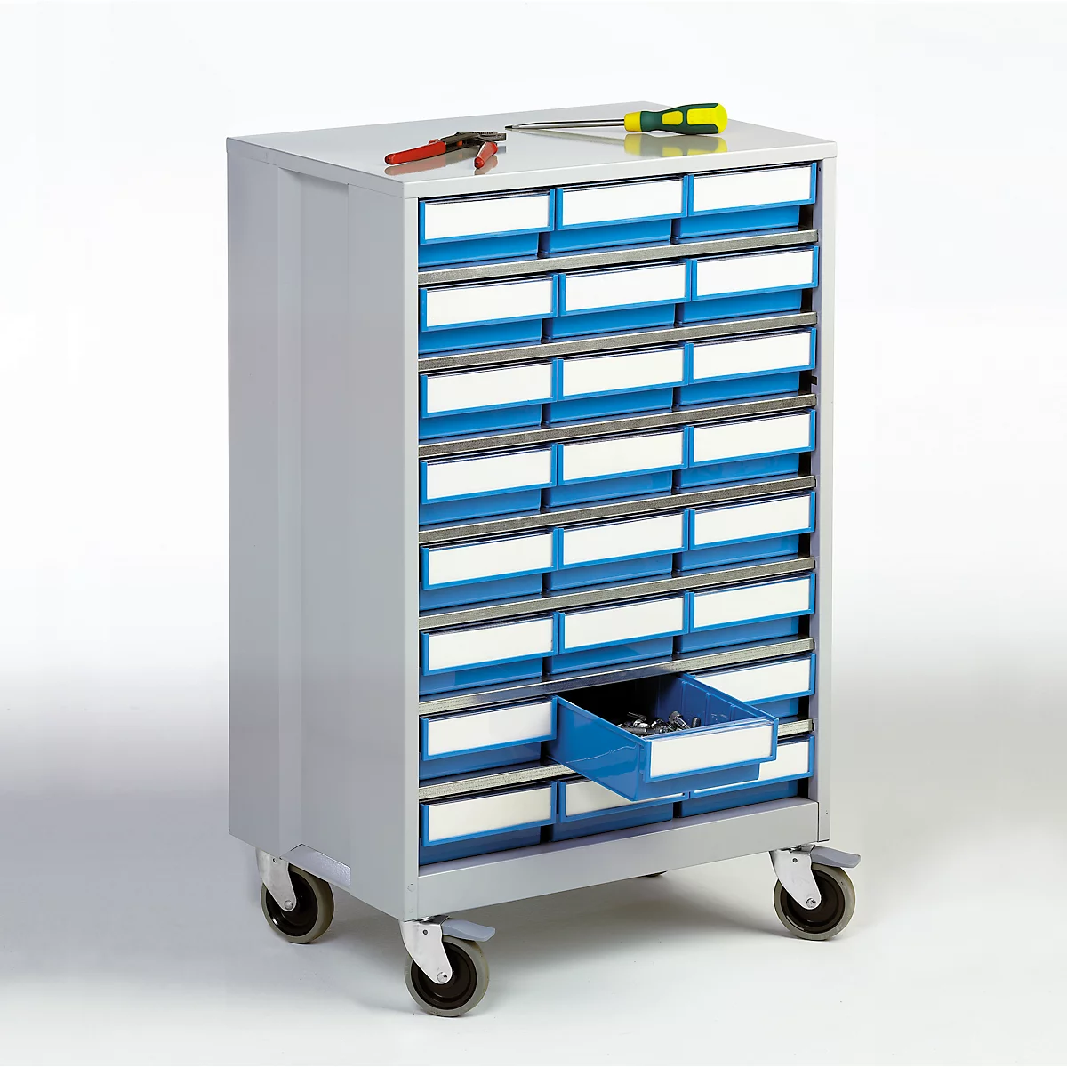 Armario de herramientas gris con cajones. En la parte superior hay herramientas como alicates y destornilladores. Un cajón está abierto.