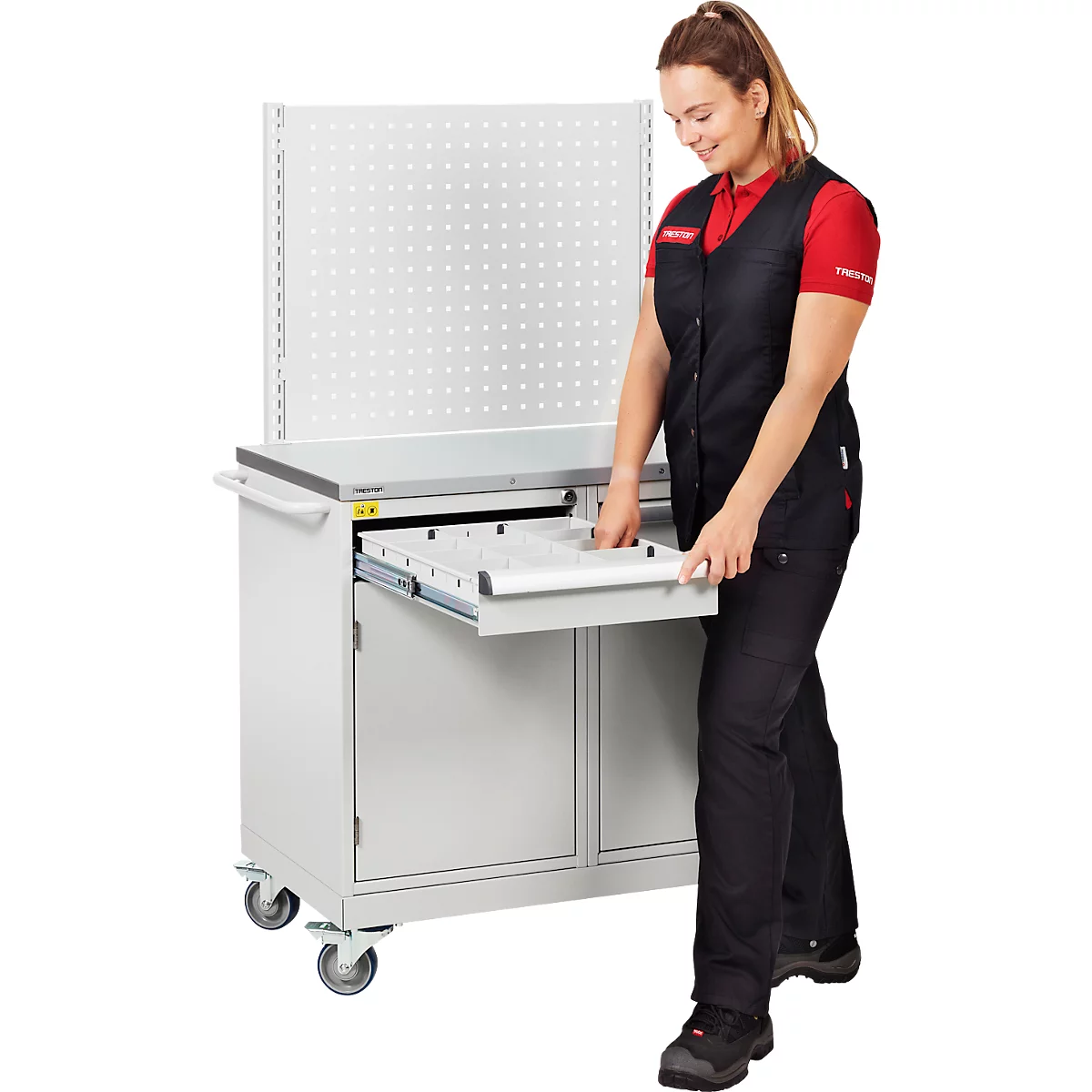 Eine Frau öffnet die Schublade eines Werkstattwagens. Der Wagen hat eine Lochwand und ein Tablett.