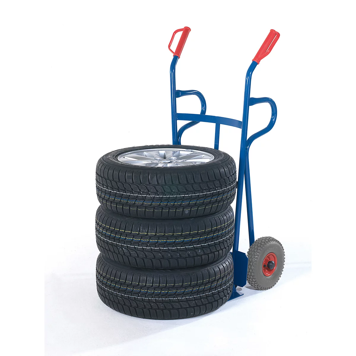 Three car tires rest on a blue hand truck with red handles. White background.