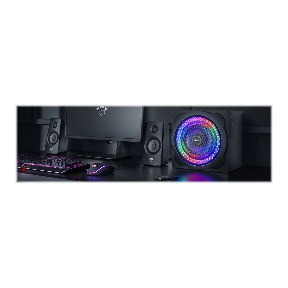 Ein schwarzes Lautsprecher-System mit RGB-Beleuchtung, Tastatur, Maus und Monitor auf einem dunklen Schreibtisch.