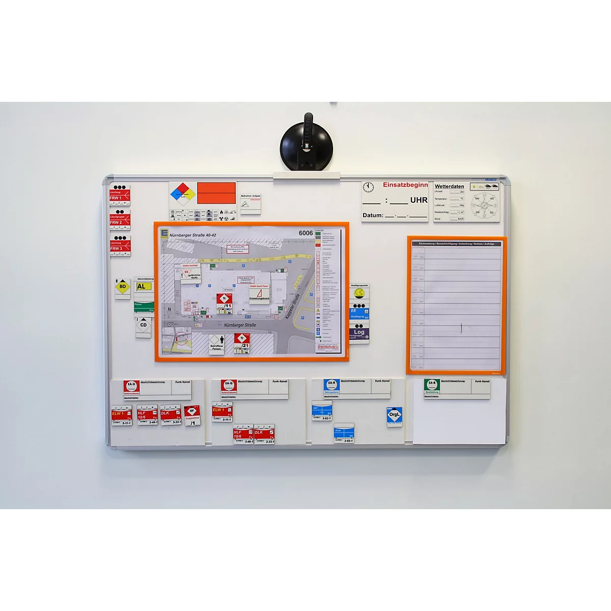 Ein Whiteboard an einer weißen Wand mit einem Gebäudeplan, Infofeldern und beschrifteten Magnetschildern für den Notfall.