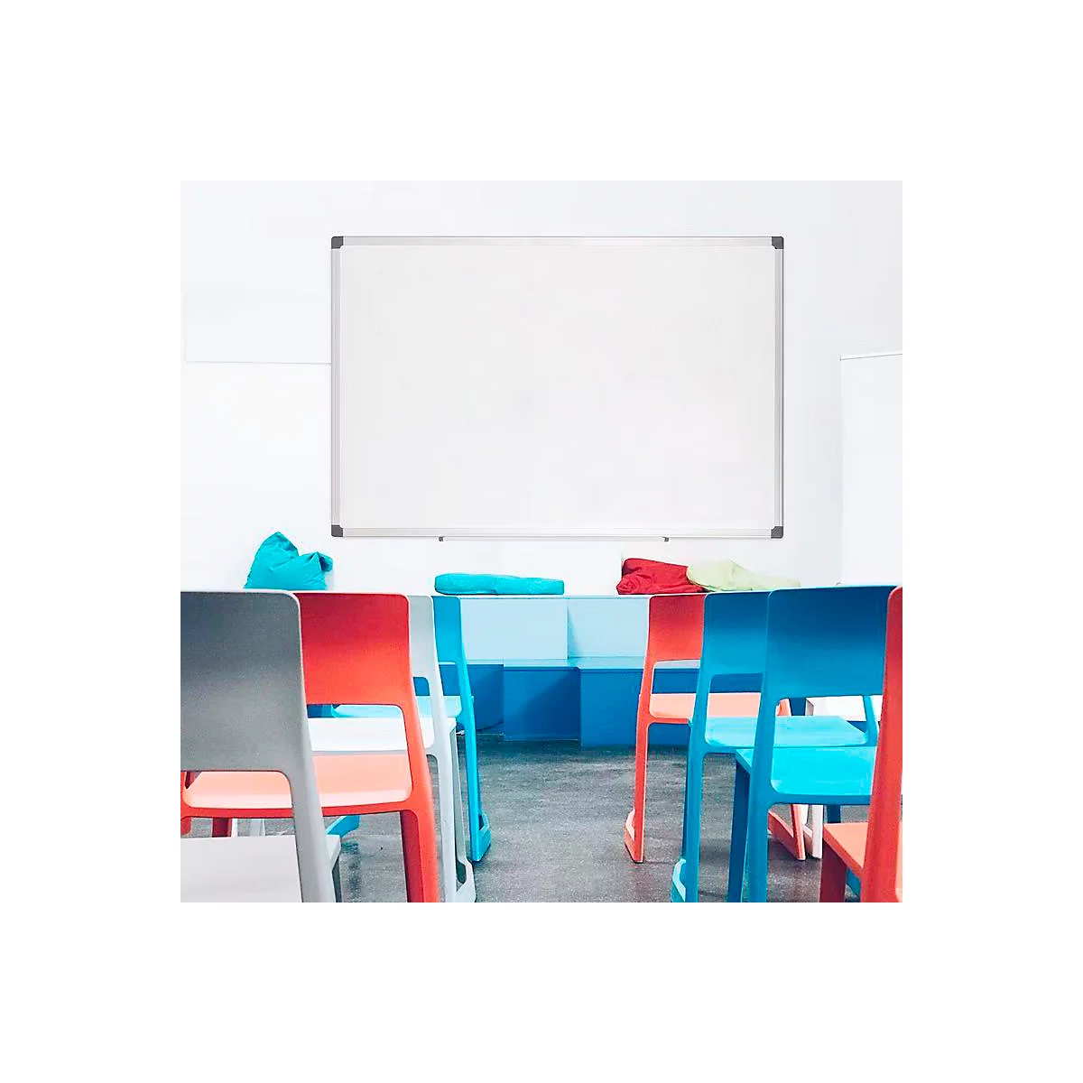 Ein Klassenraum mit weißer Tafel, bunten Stühlen und Polstern.