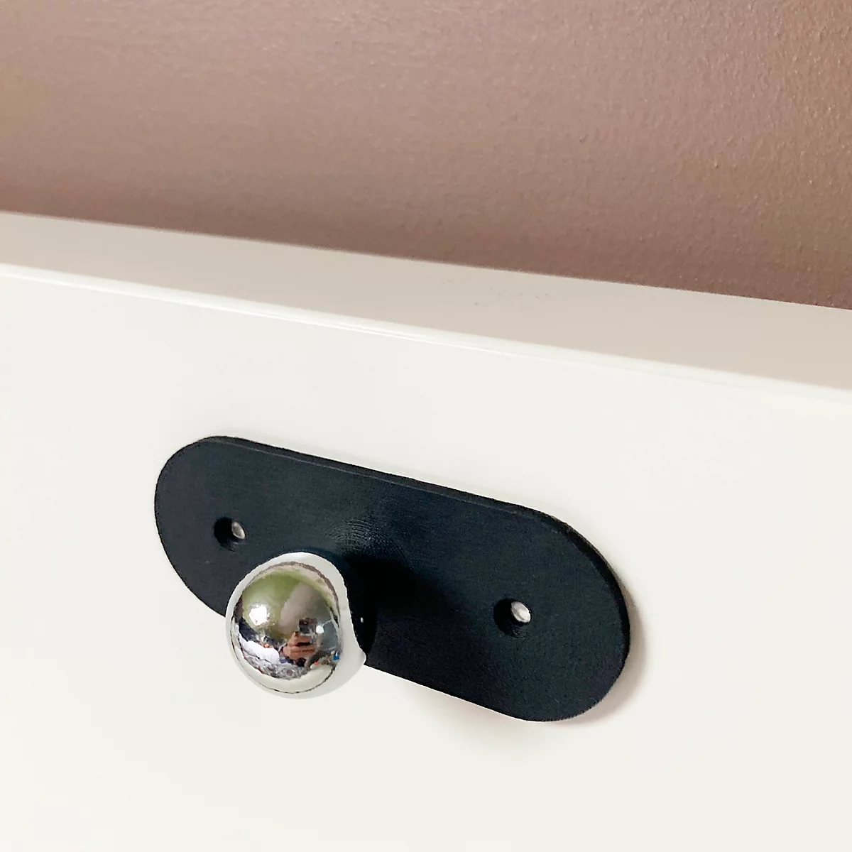 Bouton de meuble noir avec sphère chromée sur fond blanc.