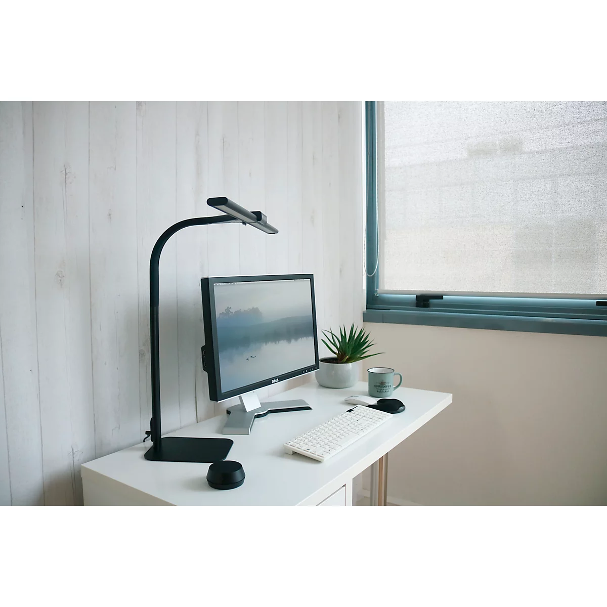 Bureau avec lampe, moniteur, clavier, souris et plante. Une fenêtre avec des stores en arrière-plan.