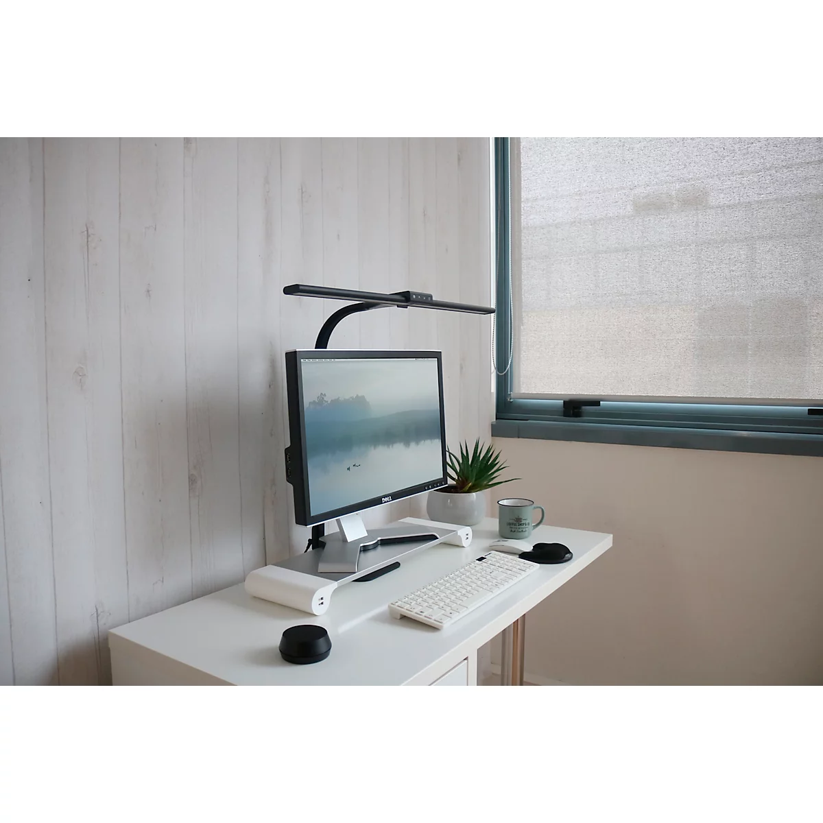 Bureau avec moniteur, clavier, lampe et plante devant des panneaux en bois.