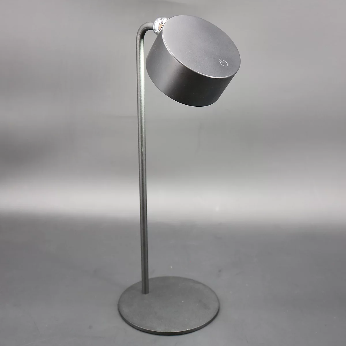 Een moderne, antracietkleurige staande lamp met een ronde voet en een cilindrische kop, gekanteld.