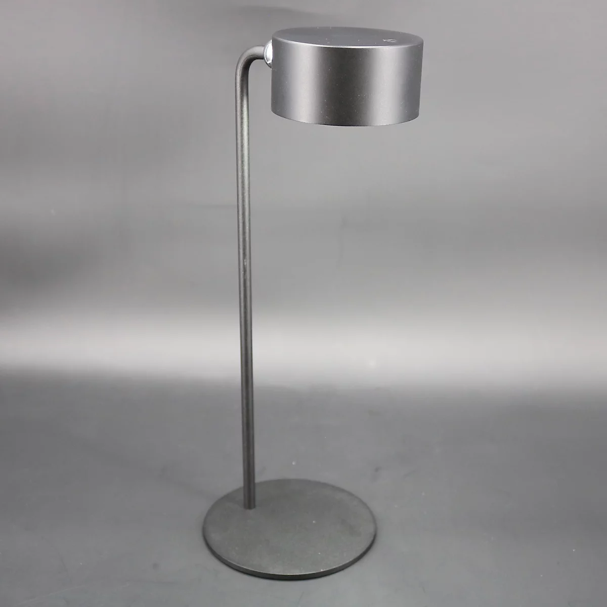 Een zilveren vloerlamp met een ronde voet, een slanke stam en een cilindrische lampenkap.