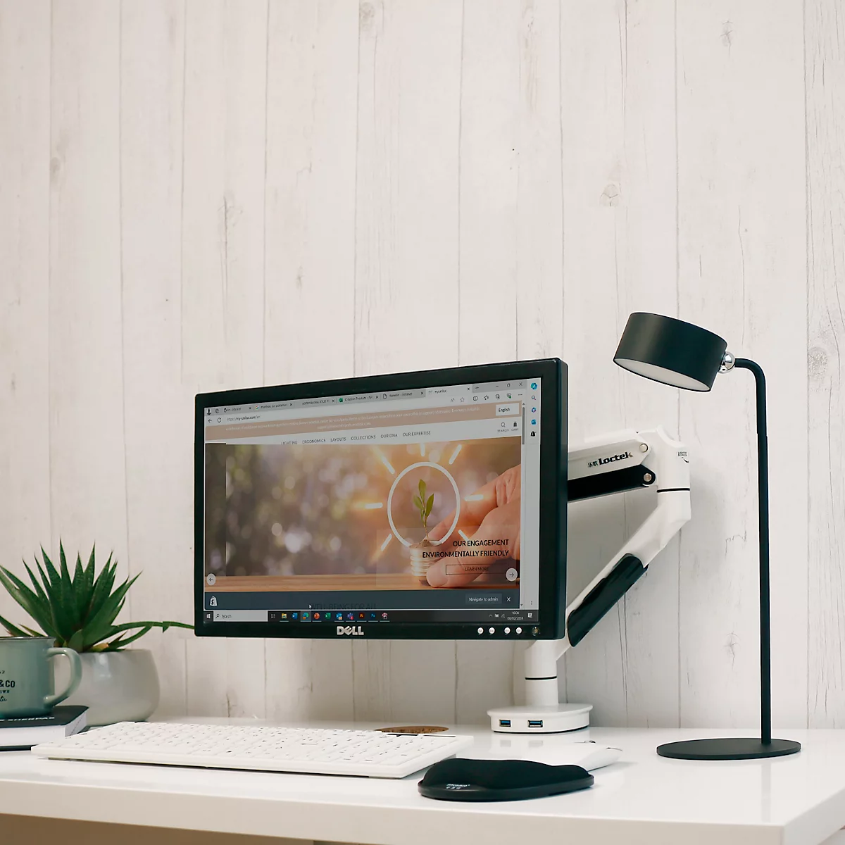 Bureau met monitor, toetsenbord, muis en lamp. De monitor toont een website met een logo.