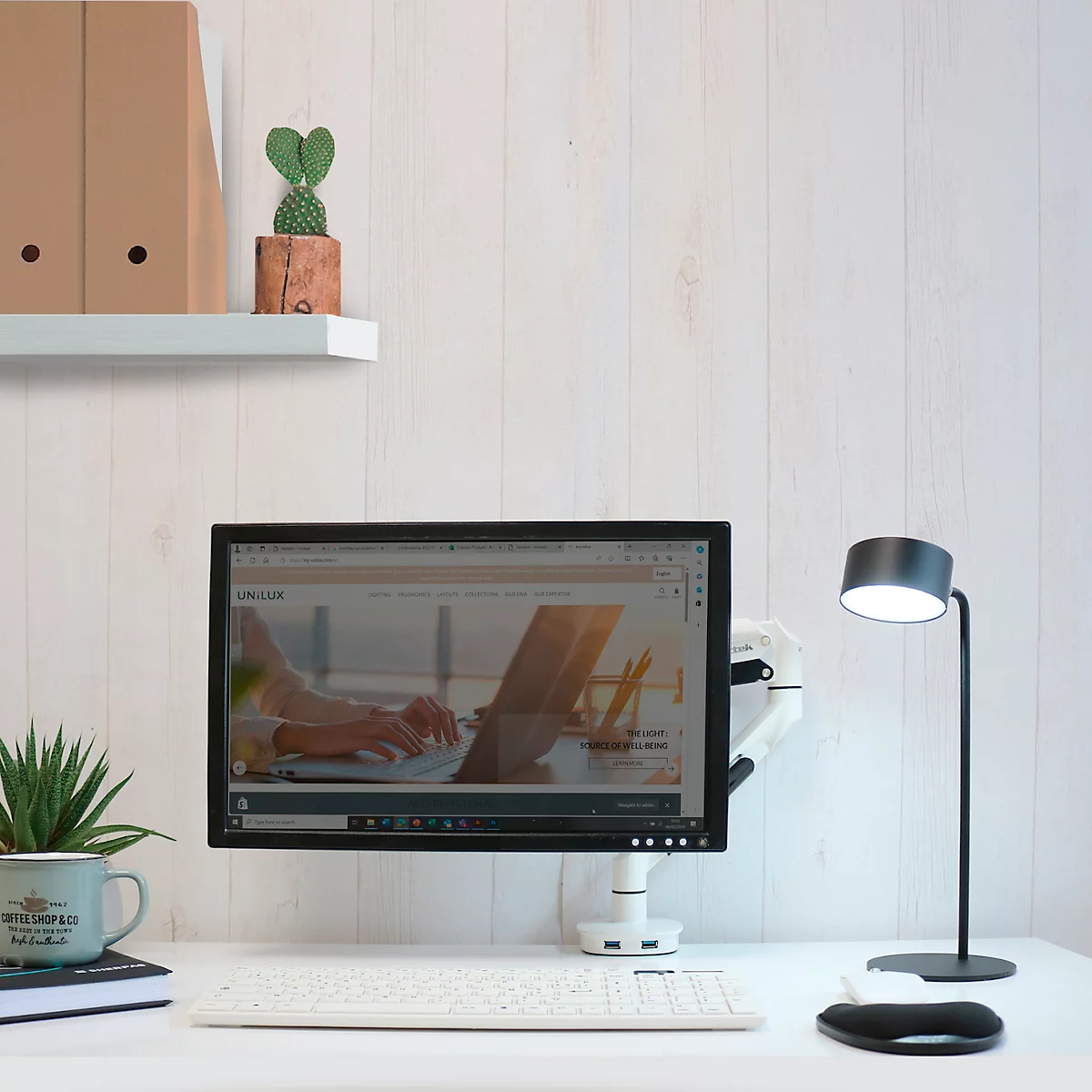 Bureau met monitor, toetsenbord, lamp en decoratie, alles tegen een witte achtergrond.