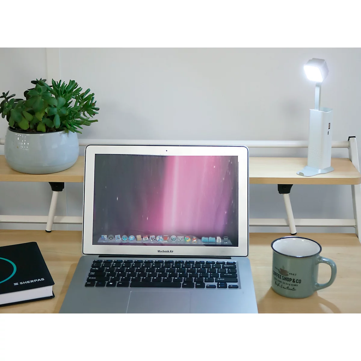 Laptop, Pflanze, Schreibtischlampe, Kaffeetasse, Buch auf einem Holztisch.