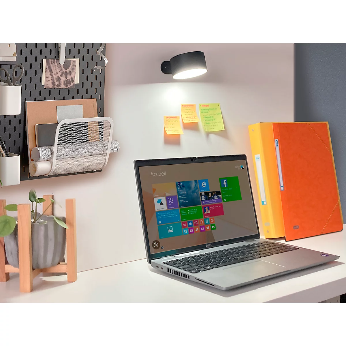 Laptop auf weißem Schreibtisch, beleuchtet von einer schwarzen Lampe. Orange Ordner und Haftnotizen daneben.