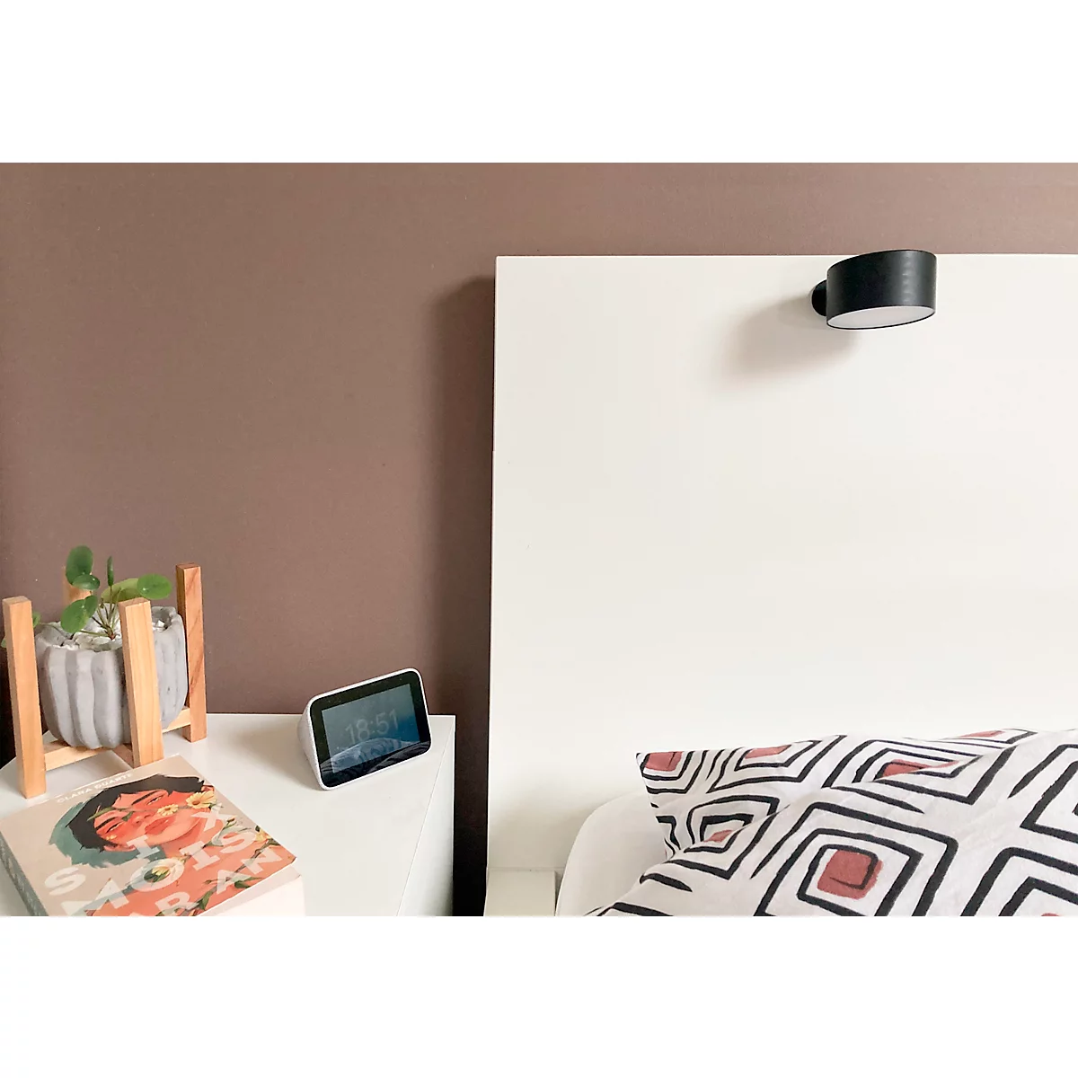 Szene eines Schlafzimmers mit Nachttisch, Pflanze, Buch und Smart Display. Kopfende und Kissen mit geometrischem Muster.
