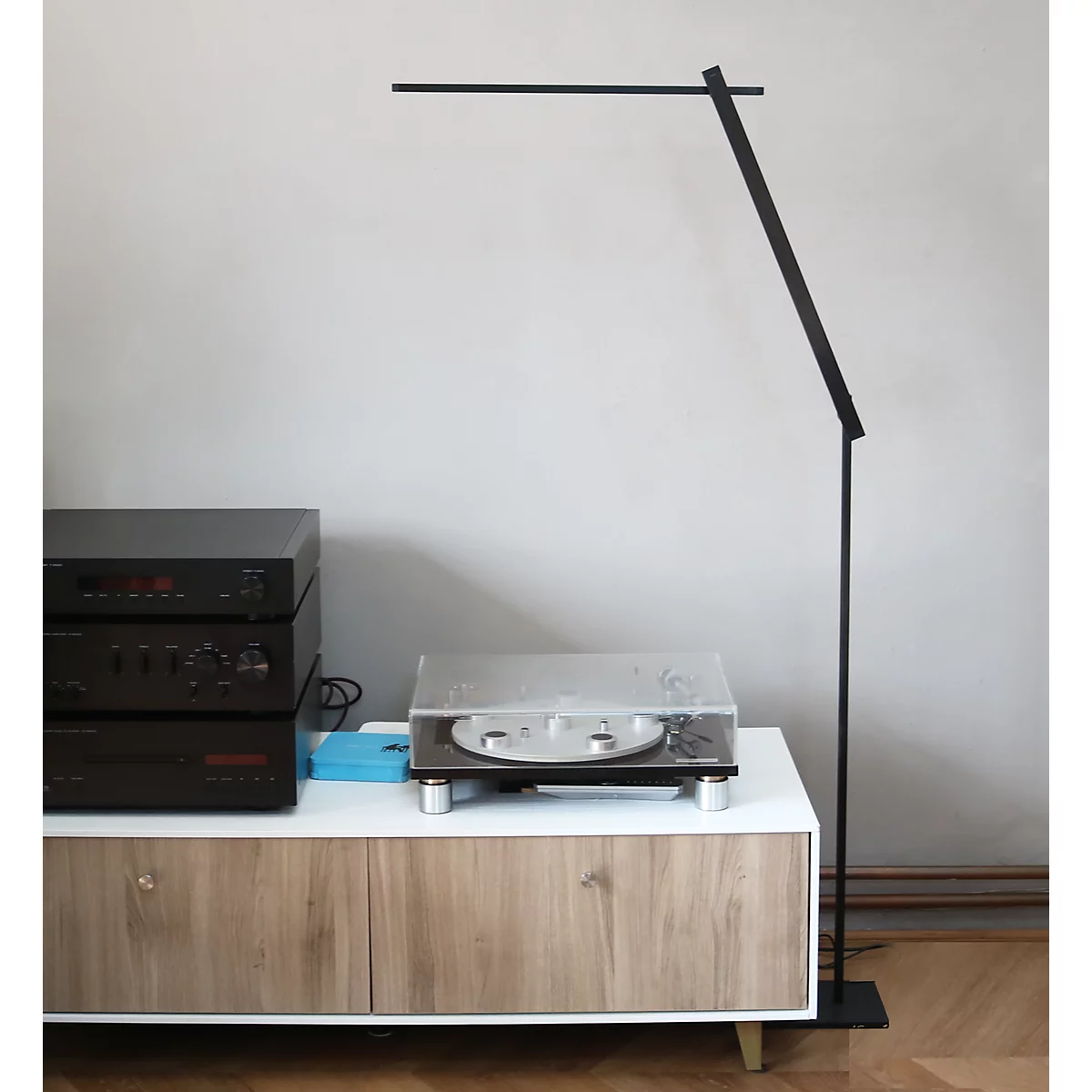 Schlanke, schwarze LED-Stehleuchte steht neben einem Sideboard mit Plattenspieler und Stereoanlage.