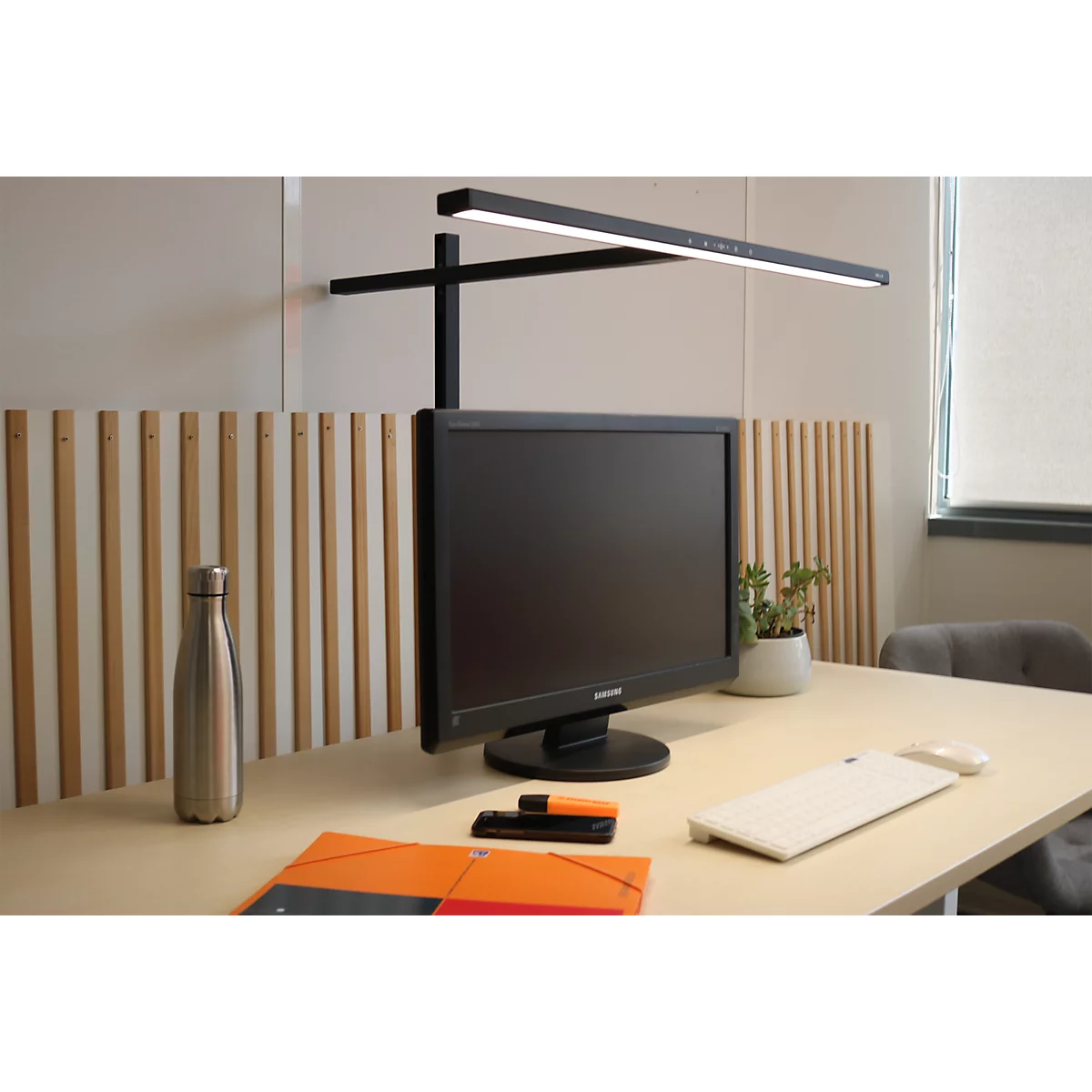 Moderne Schreibtischleuchte über einem Monitor, platziert auf einem hellen Holztisch in einem Büro.