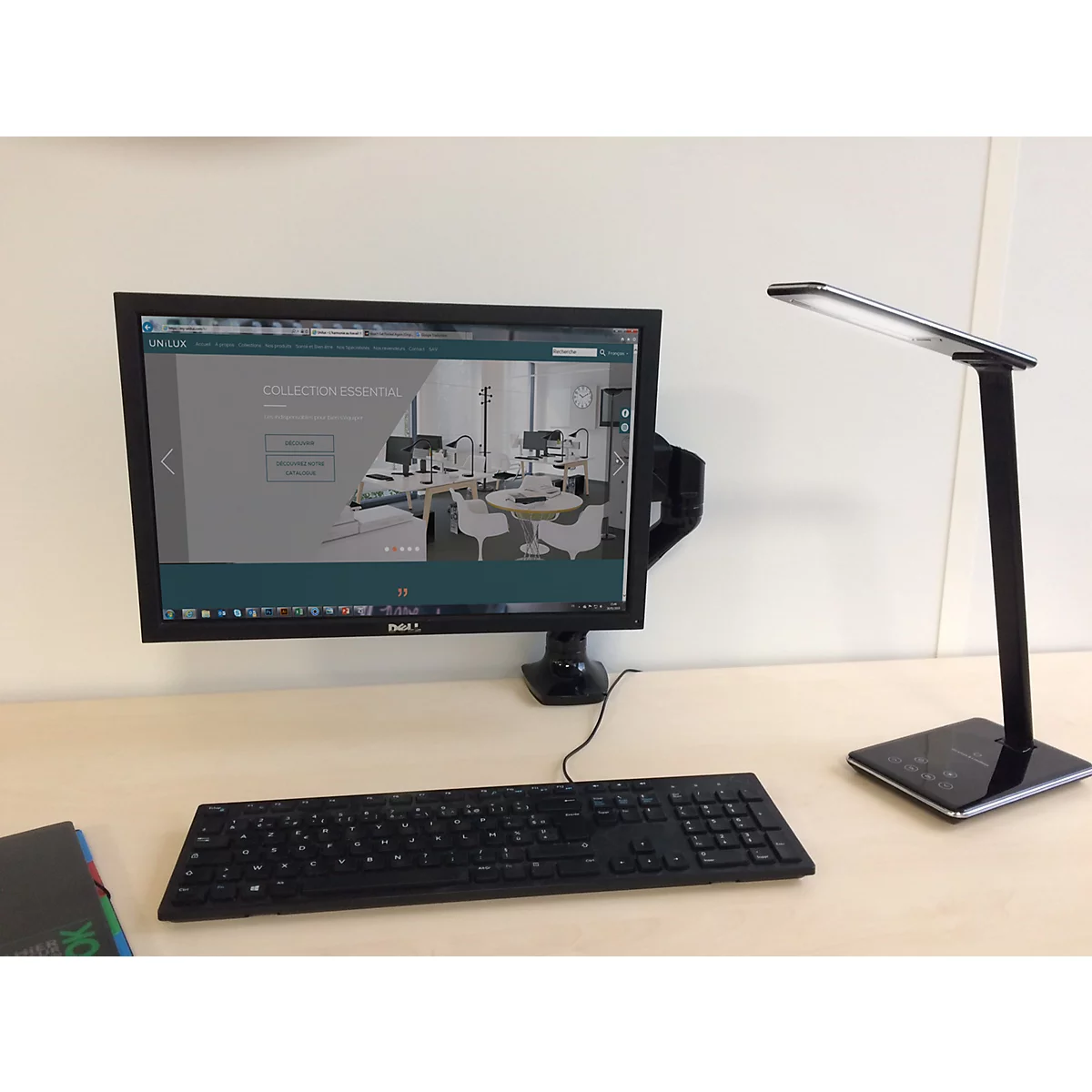 Ein moderner Schreibtisch mit Monitor, Tastatur und einer schlanken schwarzen LED-Schreibtischlampe.