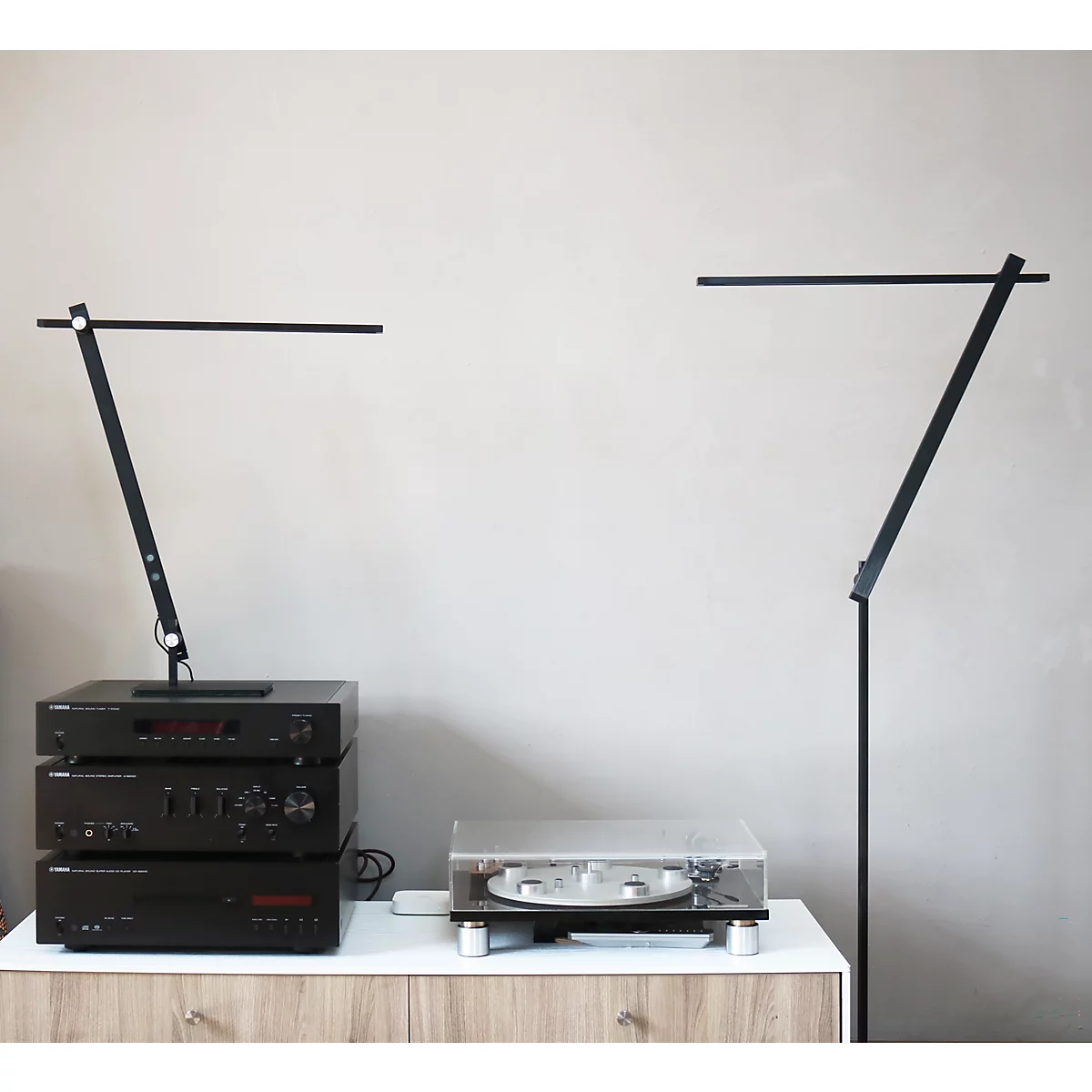 Zwei minimalistische, schwarze LED-Lampen stehen auf einem Sideboard neben einer Stereoanlage und einem Plattenspieler.