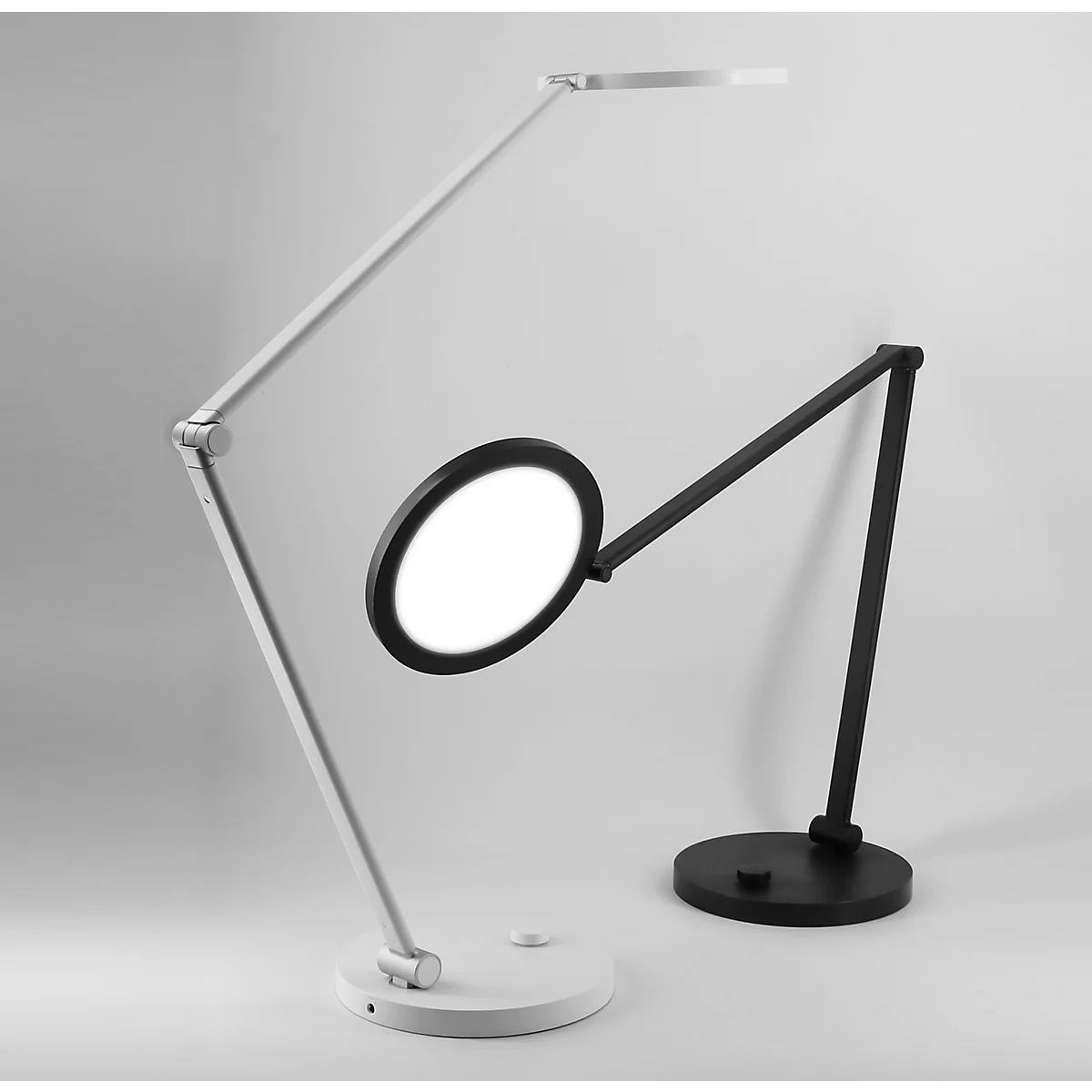 Zwei moderne Schreibtischlampen in Weiß und Schwarz mit rundem Leuchtkopf vor hellem Hintergrund.
