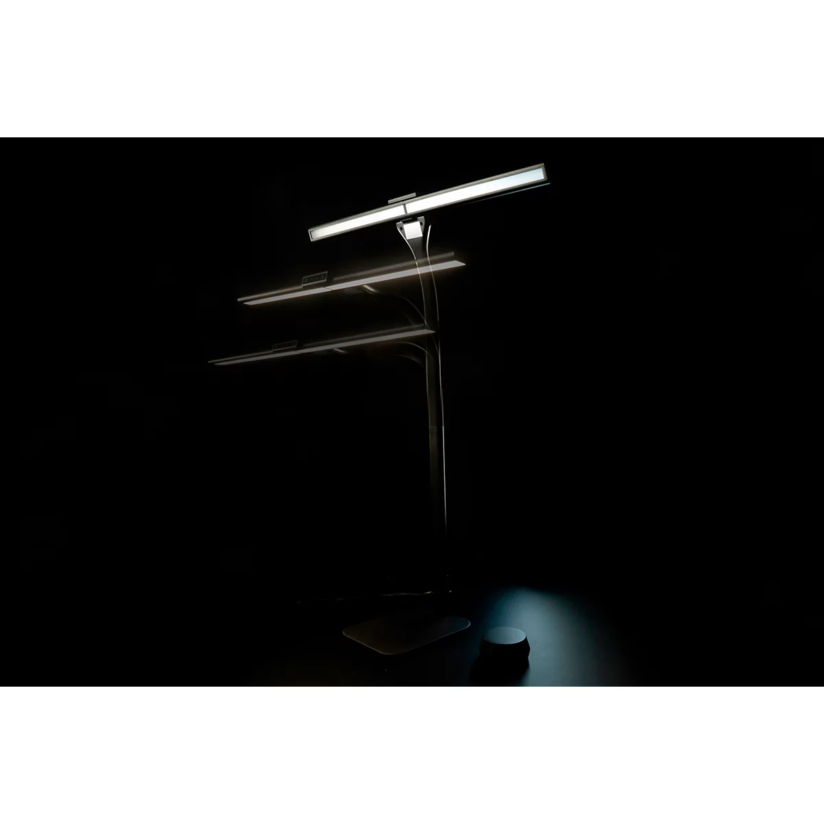 Eine elegante Schreibtischlampe mit drei Leuchtelementen vor schwarzem Hintergrund. Die Leuchten leuchten hell.