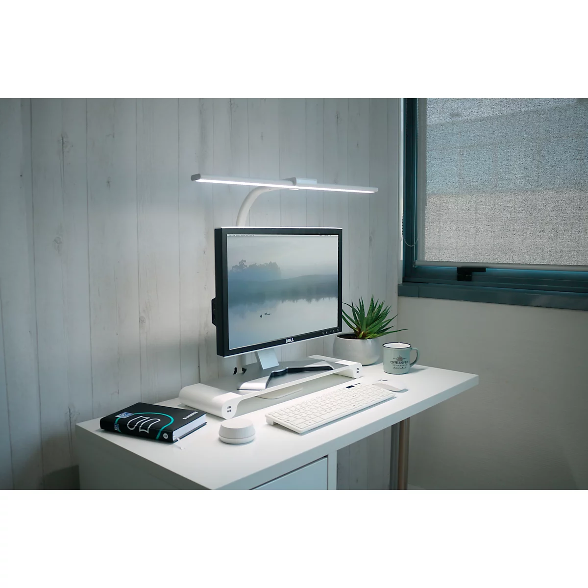Schreibtisch mit Computer, Lampe, Pflanze und Kaffeetasse. Helle, minimalistische Arbeitsumgebung.