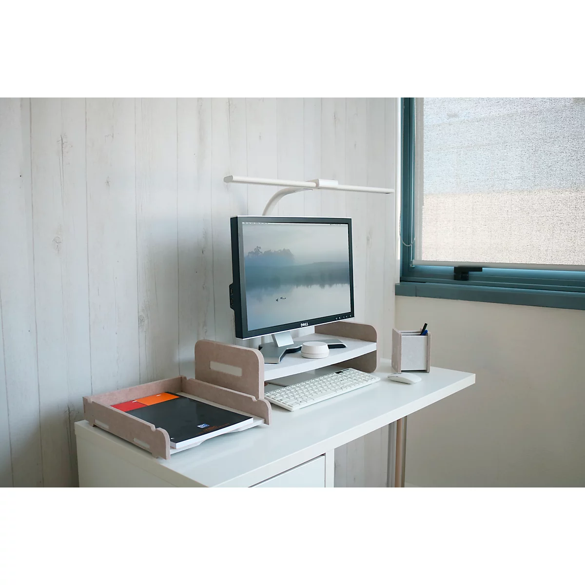 Arbeitsplatz mit Monitor, Tastatur, Ablage, Schreibtischlampe und Fenster mit Jalousie.