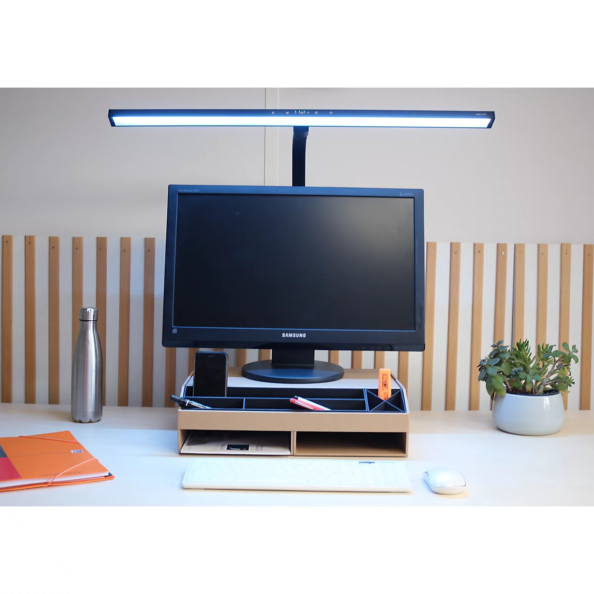 Schreibtisch-Setup mit Monitorständer aus Holz, Bildschirm und aktiver Monitorlampe.