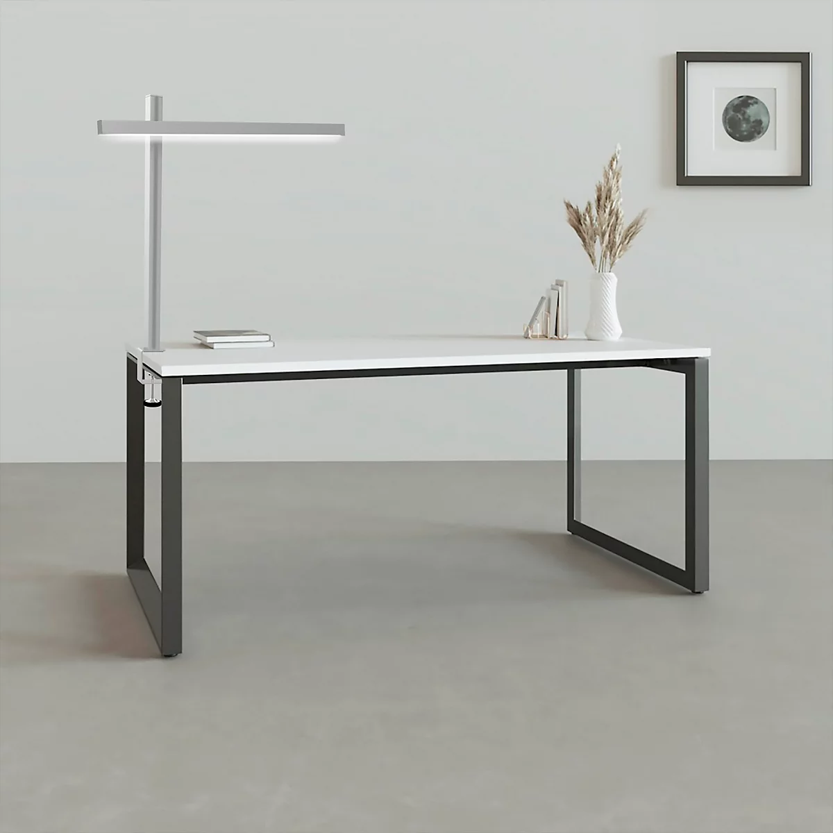 Schreibtisch mit weisser Oberfläche, schwarzem Gestell, Lampe und Deko-Elementen.