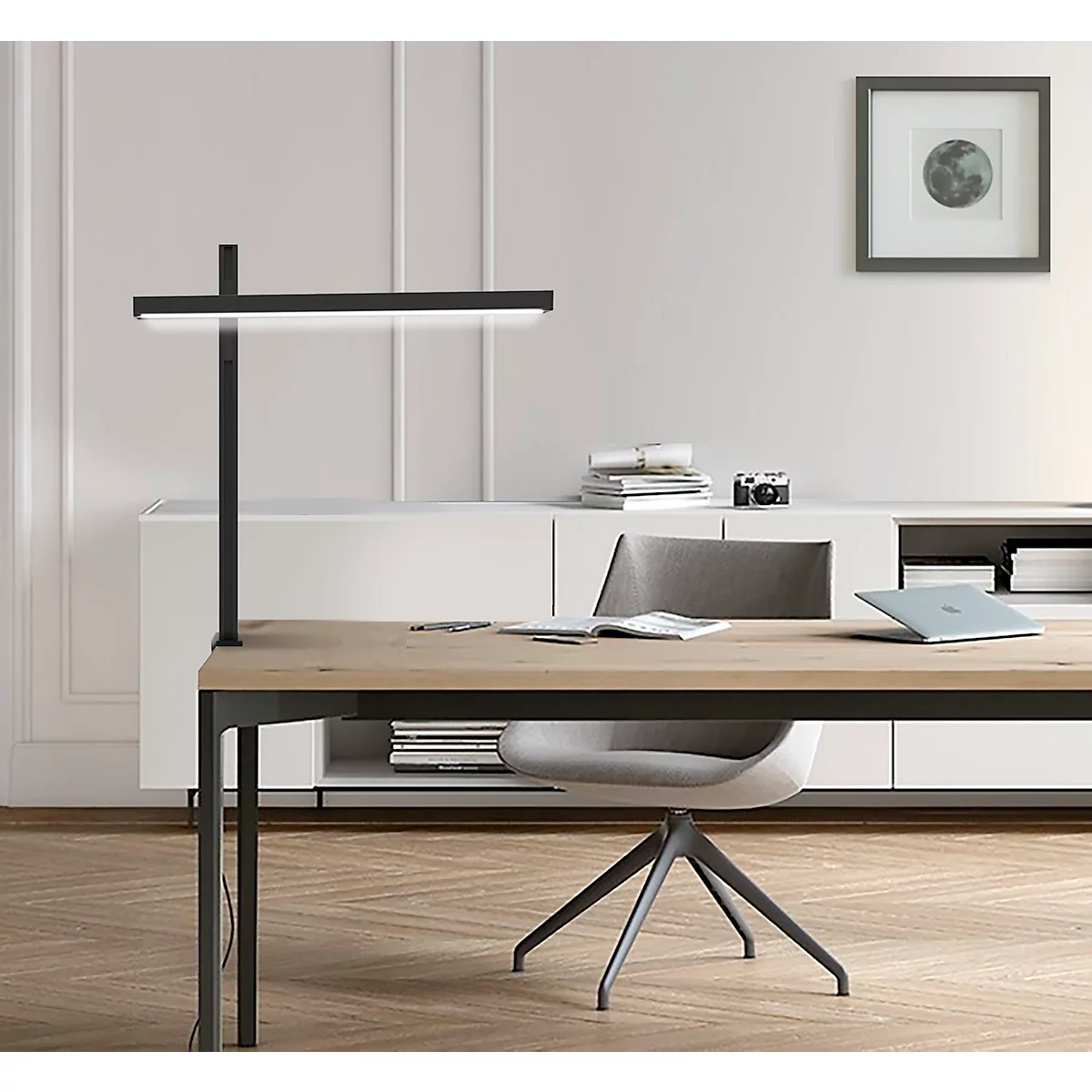 Schreibtisch mit Lampe, Laptop, Stuhl und Wandbild, helle Szene.