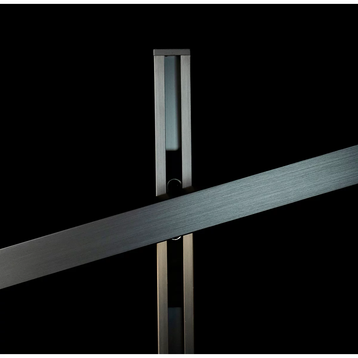 Detail einer Metallkonstruktion, bestehend aus einem senkrechten Ständer und einem diagonal verlaufenden Balken, beide vor schwarzem Hintergrund.