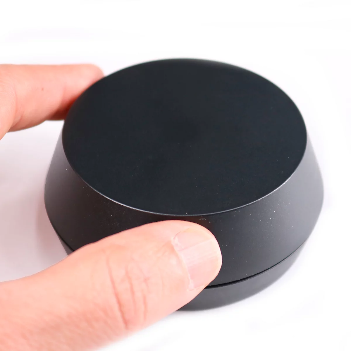 Hand houdt een zwart, rond, kegelvormig object vast op een witte achtergrond.