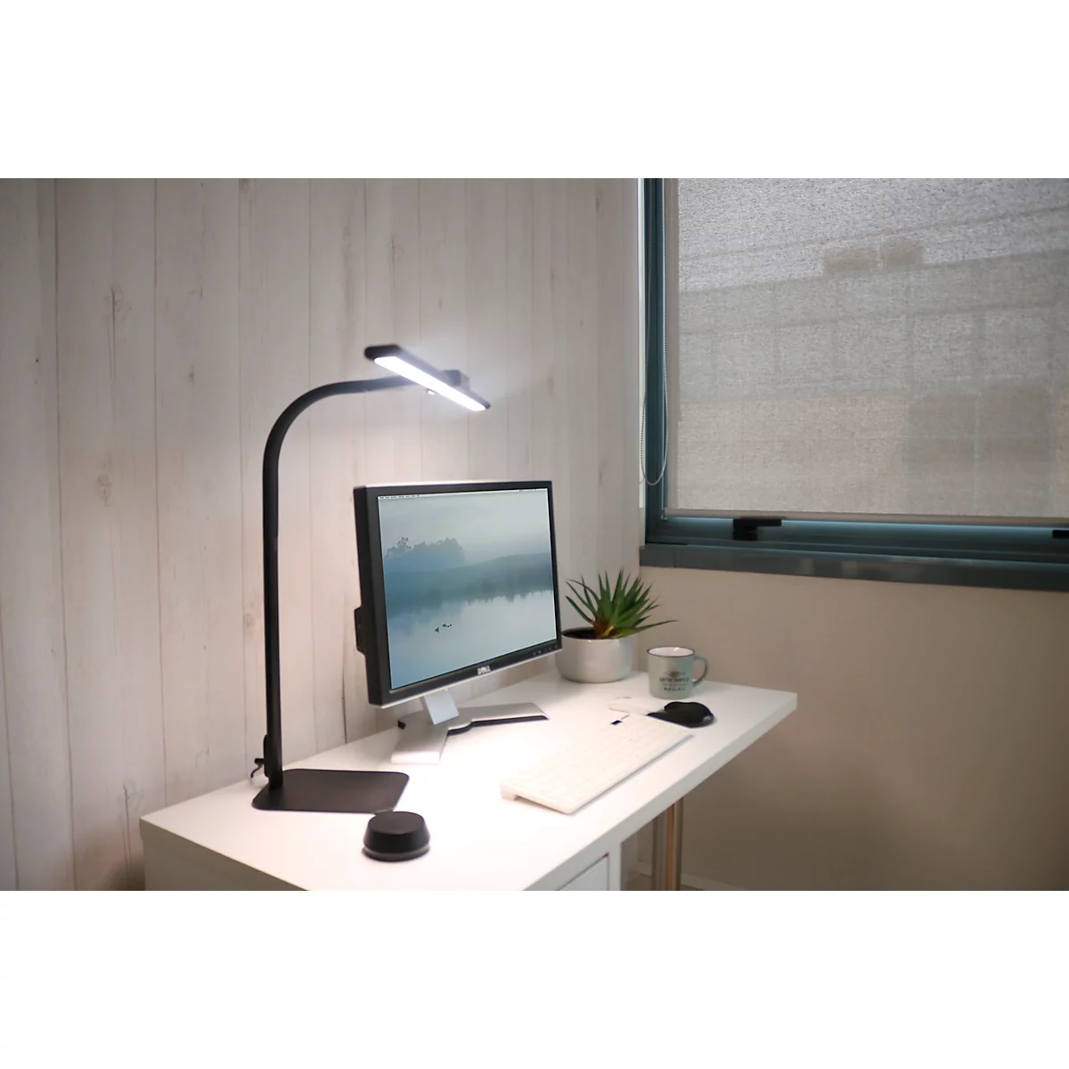 Bureau met lamp, monitor, laptop en plant. Helder kantoor met raam en jaloezieën.