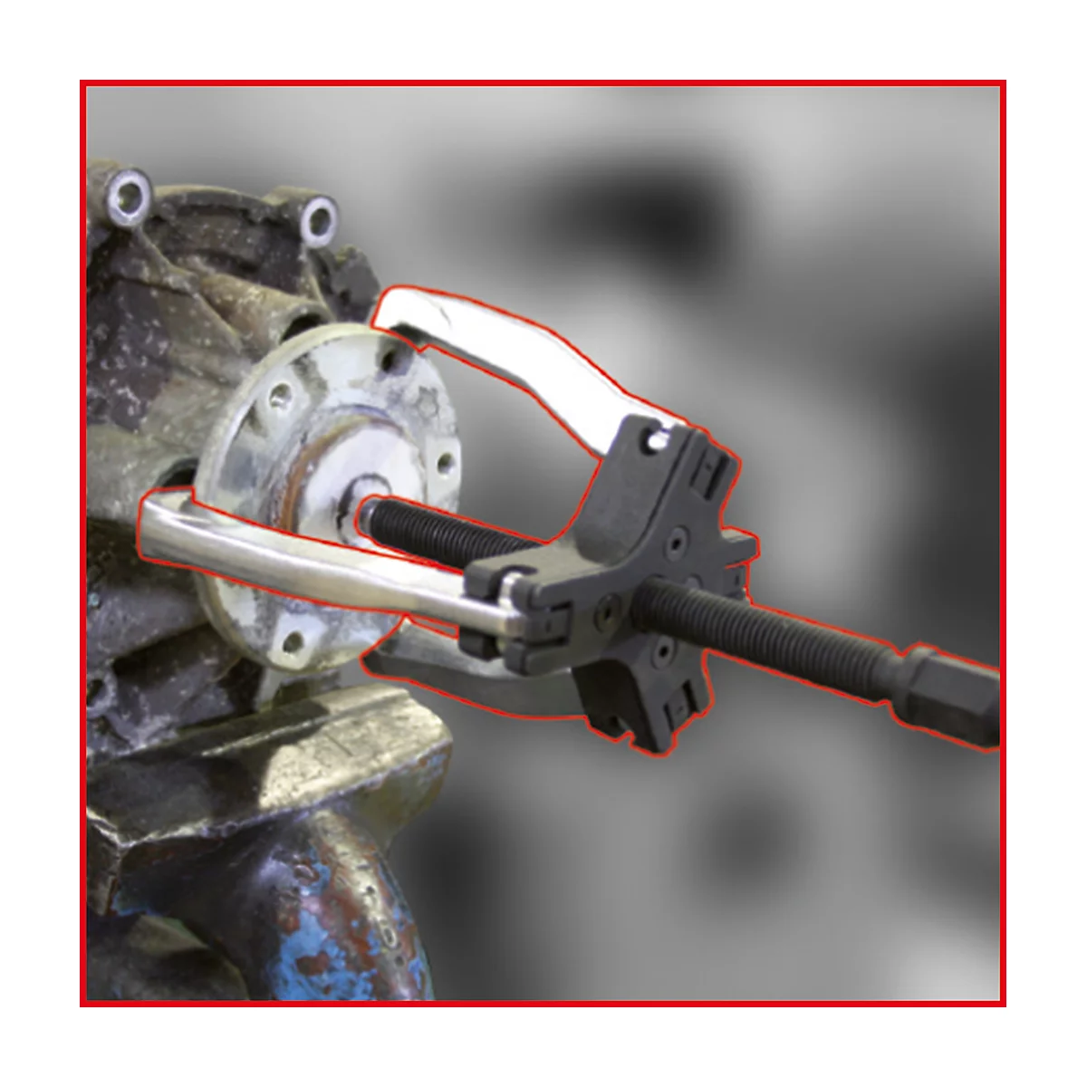 Ein silbernes Werkzeug greift in ein mechanisches Bauteil. Der Hintergrund ist unscharf.