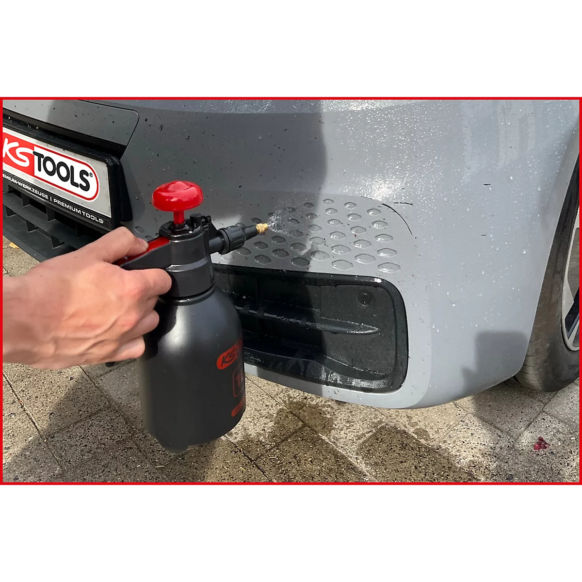 Person besprüht graue Fahrzeugstoßstange mit einer schwarzen Sprühflasche. Links ein KS TOOLS-Logo.