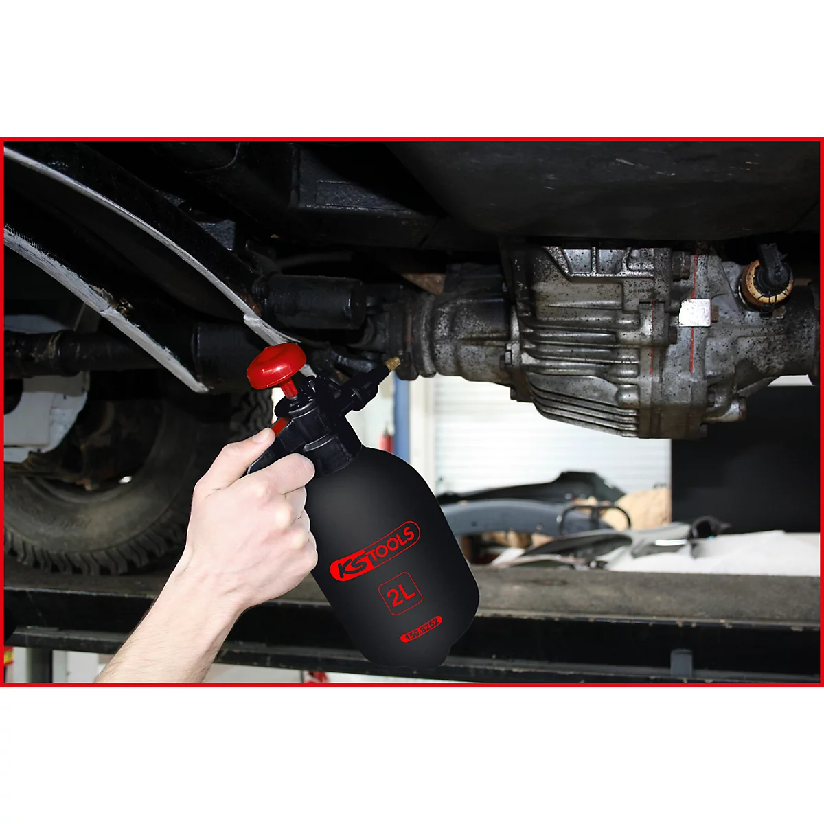 Person besprüht Fahrzeugunterboden mit einer schwarzen Sprühflasche. Aufschrift: KS TOOLS, 2L.