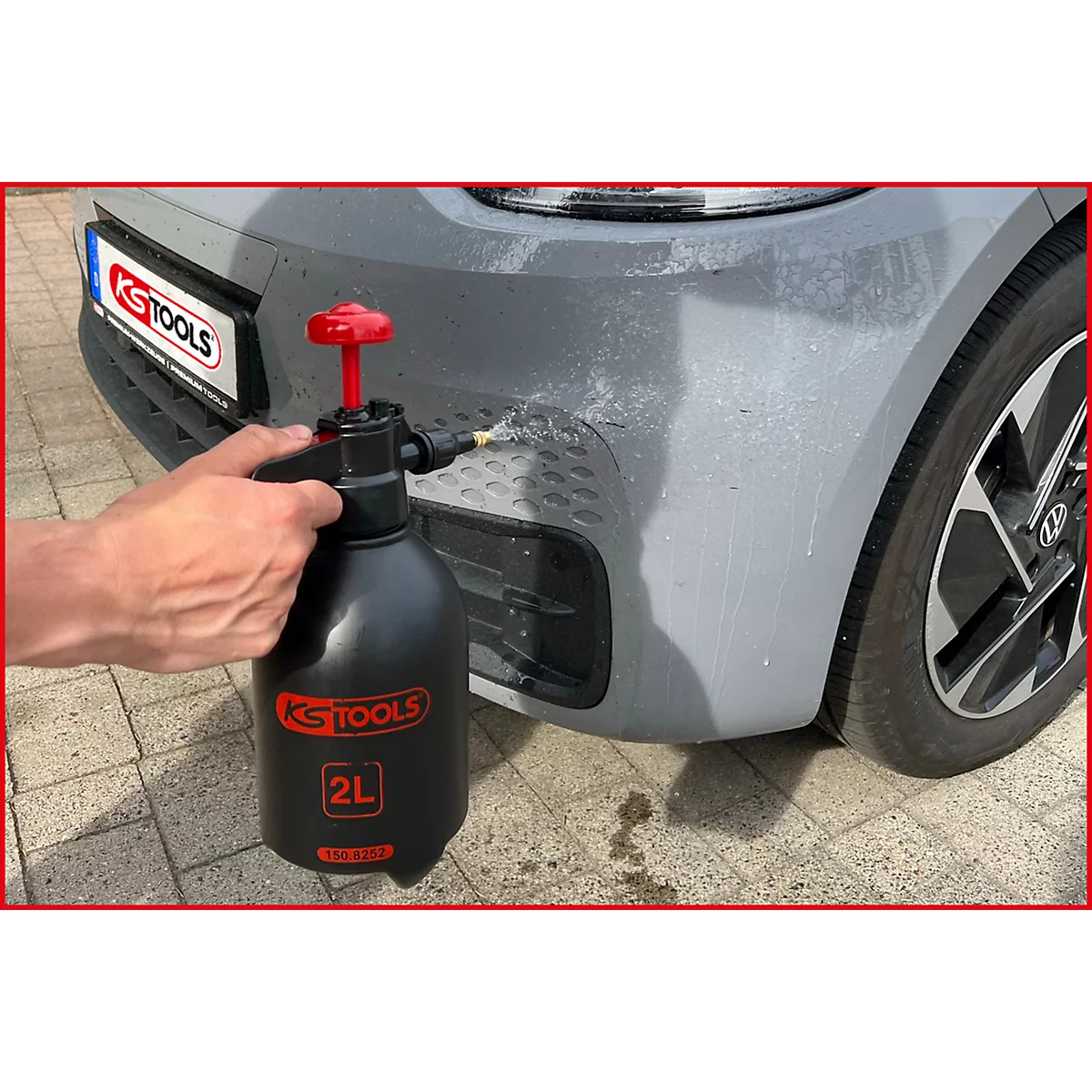 Person sprüht Auto mit schwarzer KS TOOLS Sprühflasche ein. Rotes Ventil, Schriftzug, 2L.