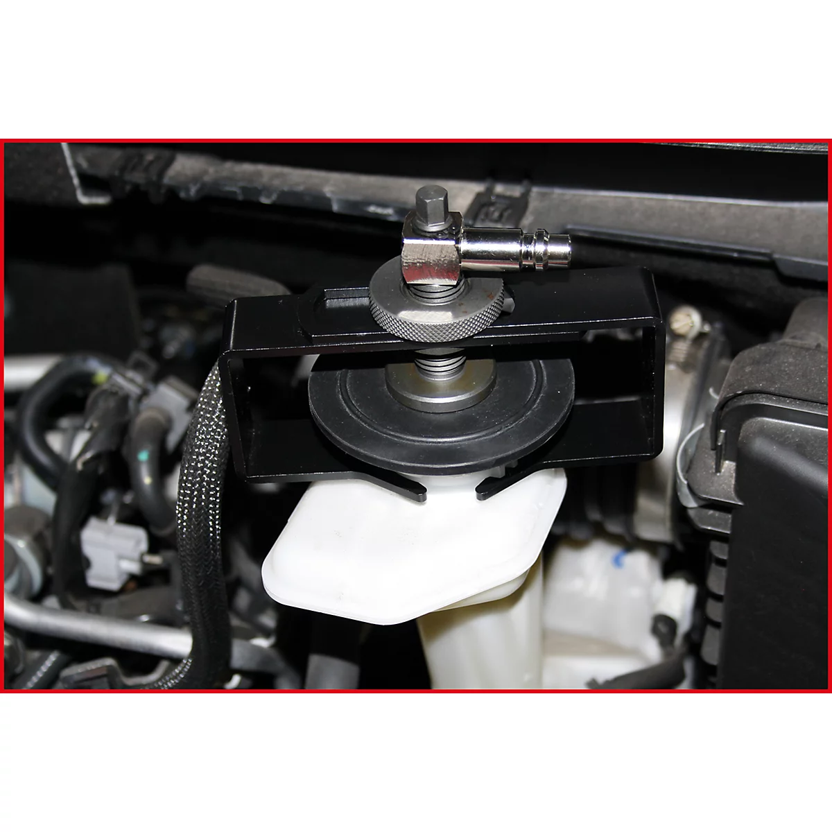 Detailaufnahme: Werkzeug an einem Motorraum, an einer weißen Flüssigkeitsbehältervorrichtung befestigt. Schwarz, Metall, grau.