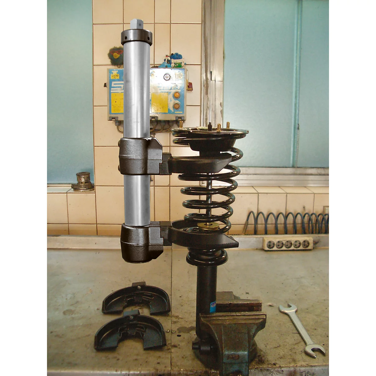 Ein Stoßdämpfer-Set wird in einer Werkstatt zusammengebaut. Auf dem Tisch liegen Bremssättel und ein Schraubenschlüssel.