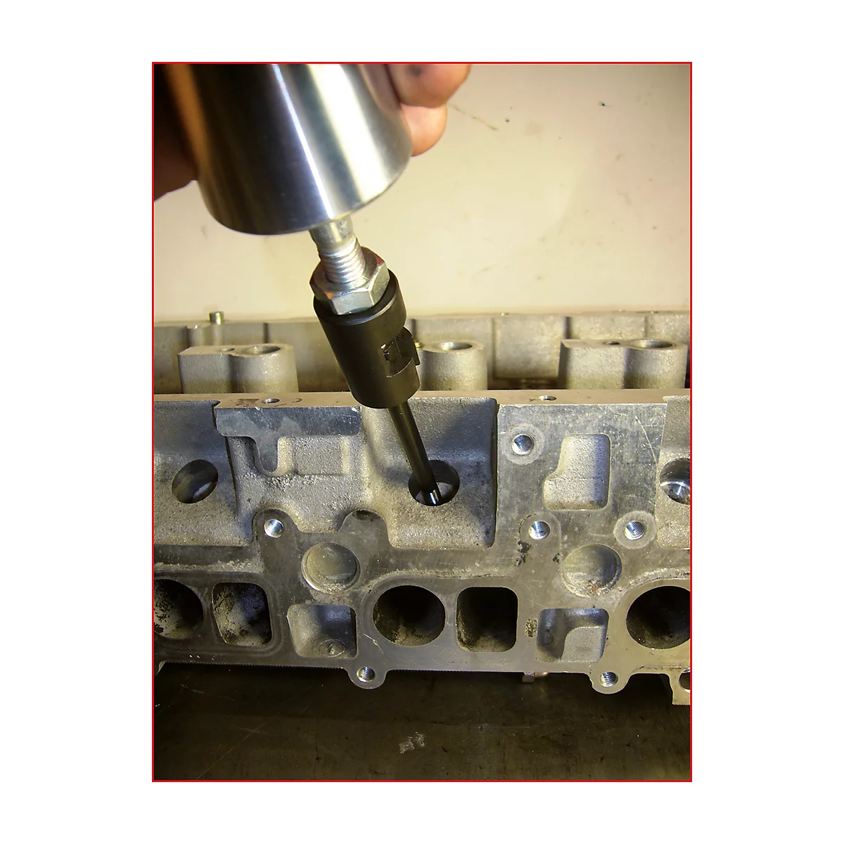 Eine Hand hält ein Werkzeug, das in ein Loch eines Metallblocks eingeführt wird. Der Hintergrund ist unscharf.