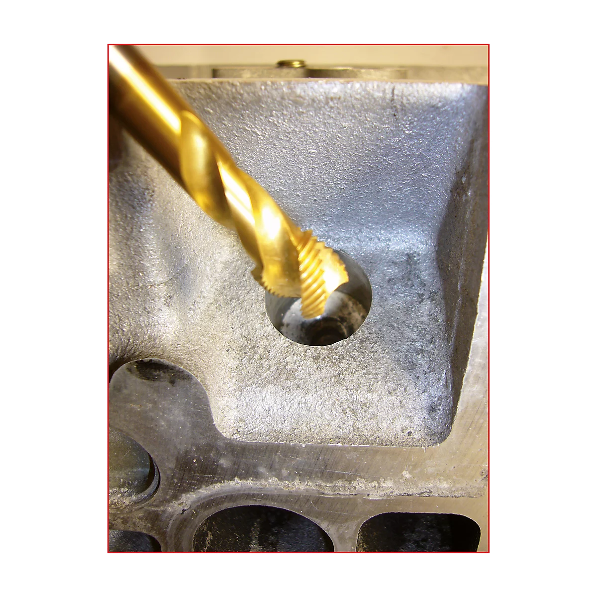 Nahaufnahme eines goldfarbenen Bohrers, der in ein Loch in einem grauen Metallblock bohrt.